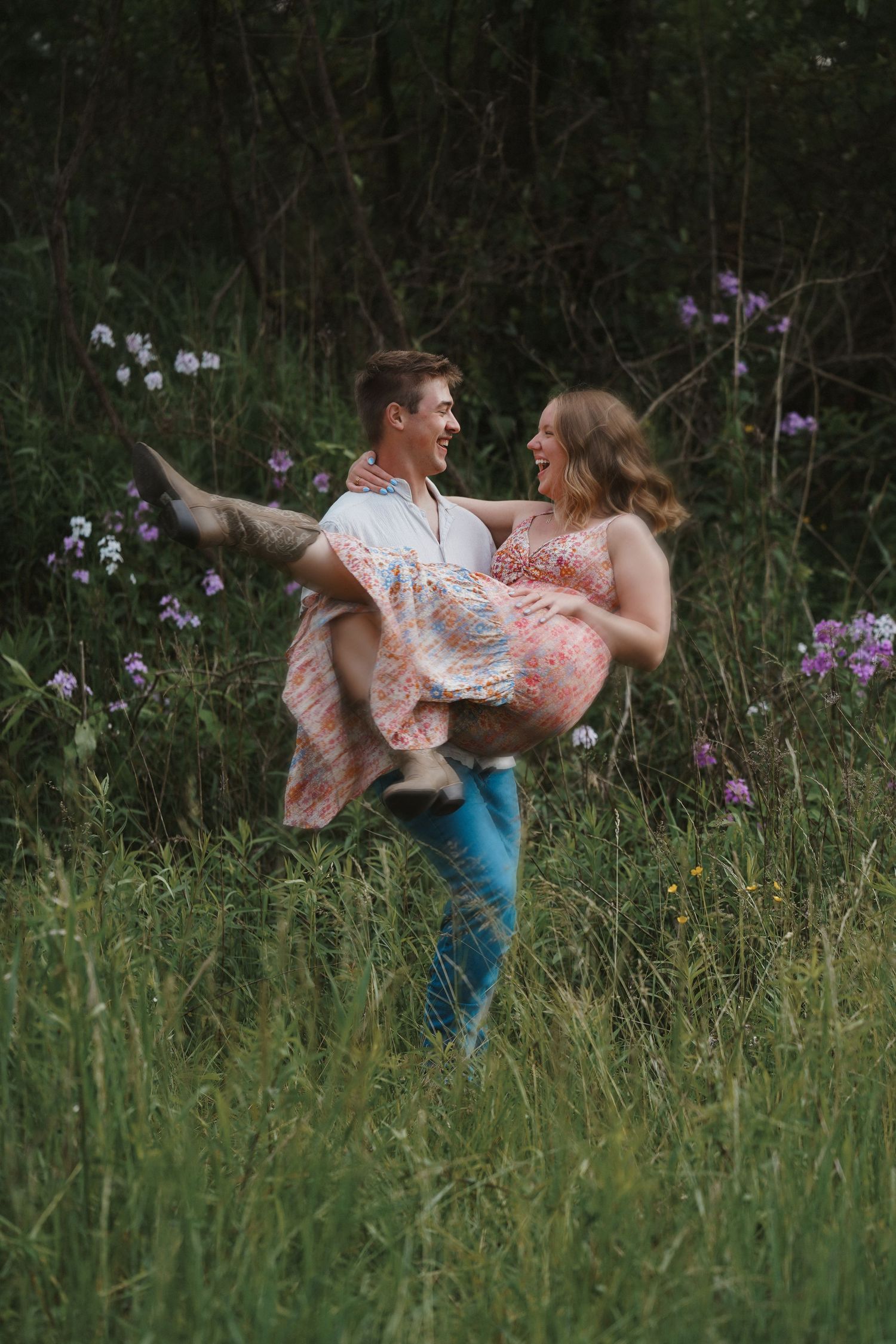 A romantic couple embraces in a meadow with purple wildflowers during a tender summer moment.