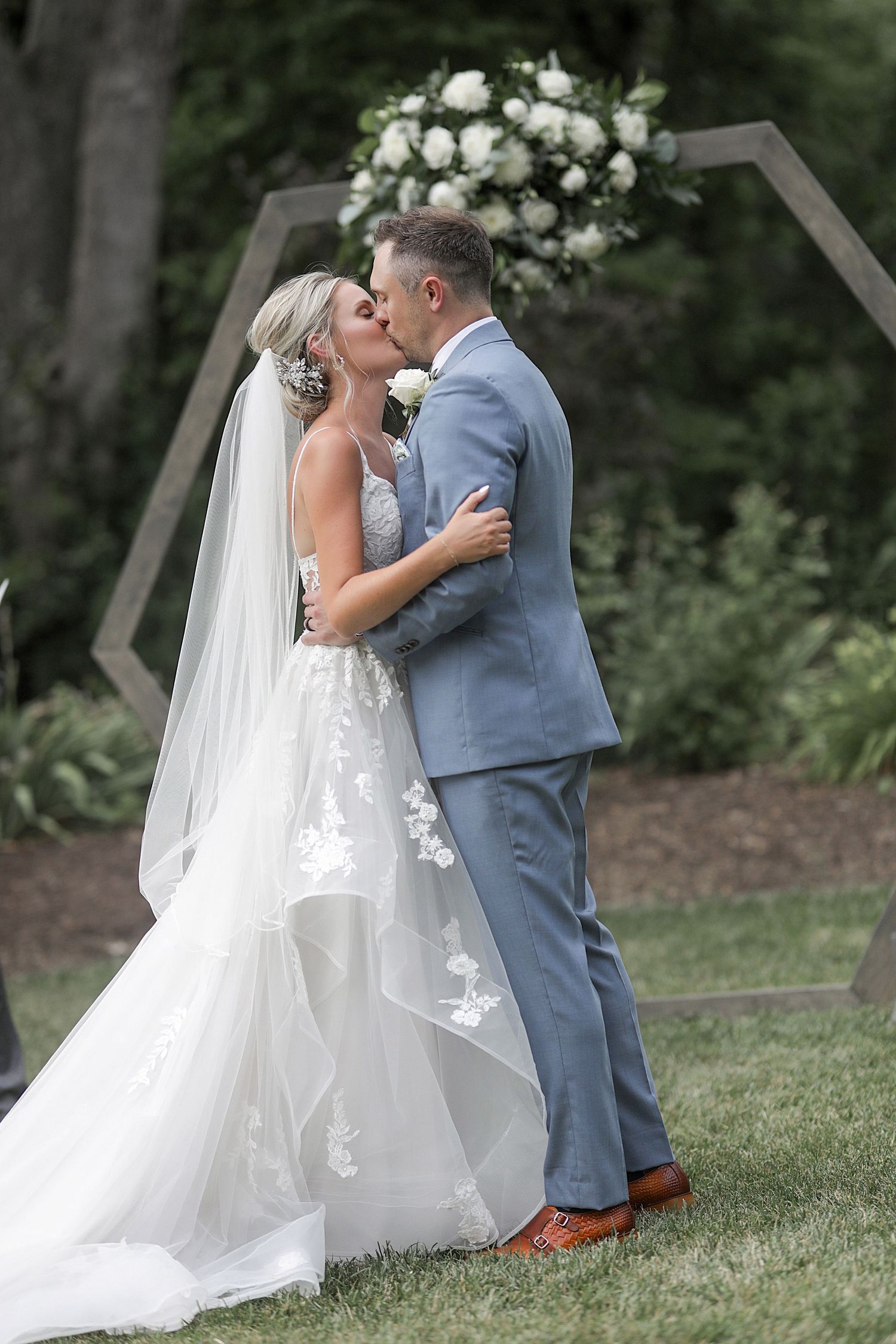 Wedding couple embracing during outdoor photo session on grassy hillside.