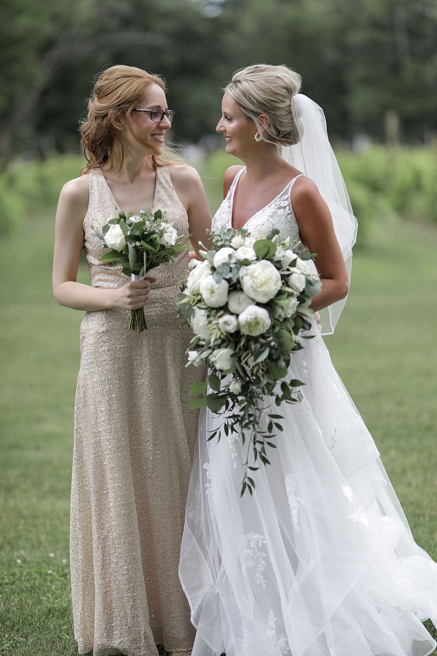 Bride and bridesmaid sharing joyful moment with elegant white bouquets outdoors.