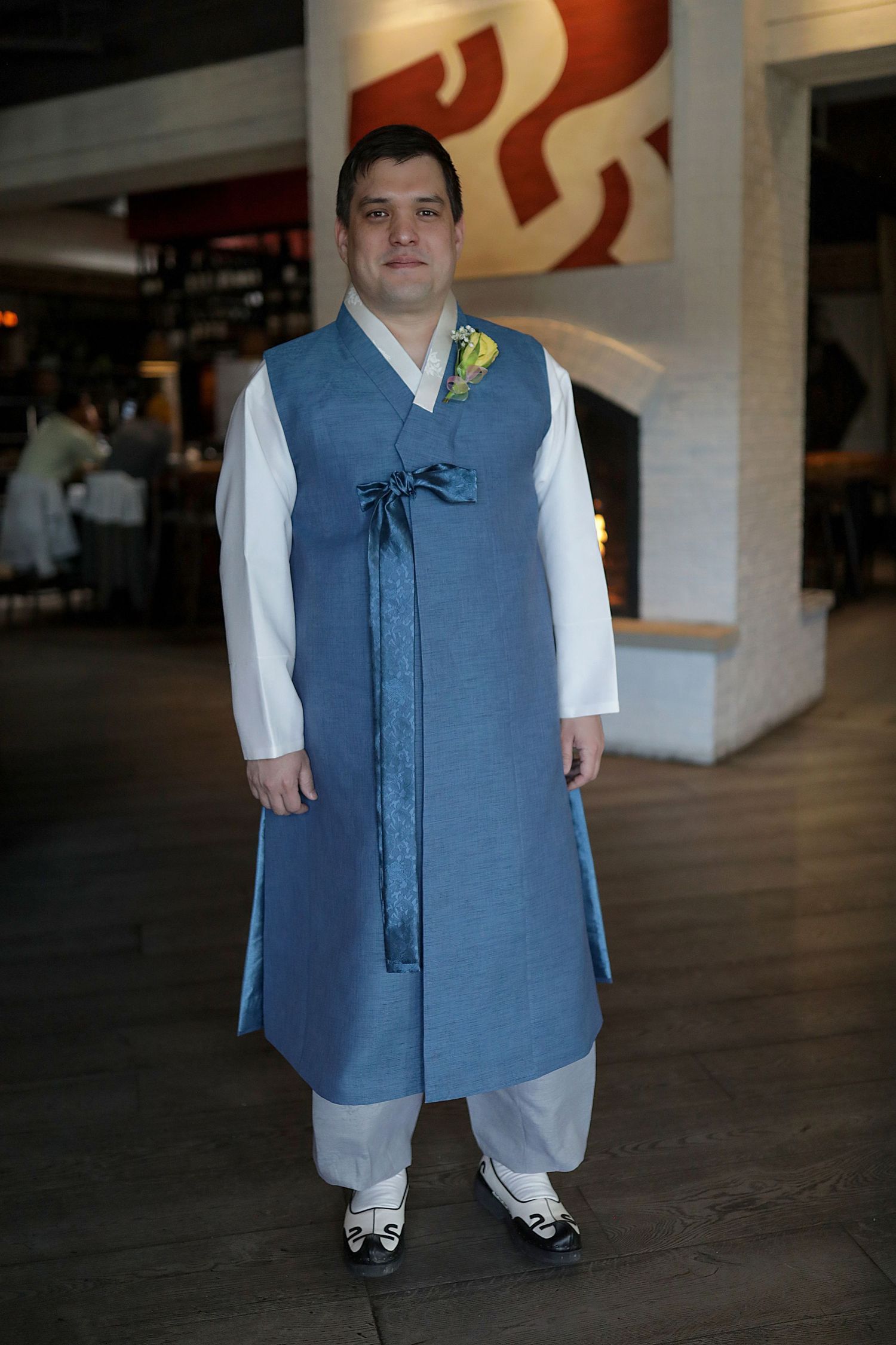 A person wearing a blue vest over a white shirt stands in a dimly lit interior space.