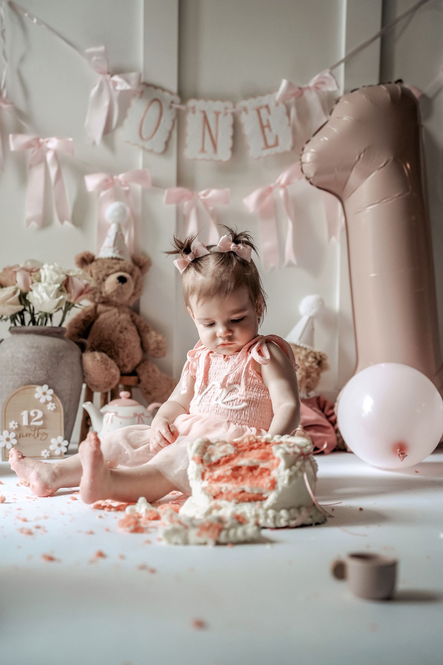 A series of photos showing pink cake smash session with frosting and teddy bears against a white backdrop with banner decor.