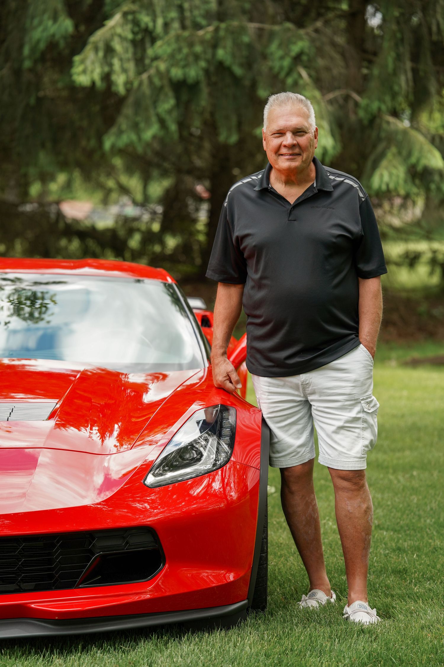 A bright red Chevrolet Corvette sports car parked on grass with greenery in the background.