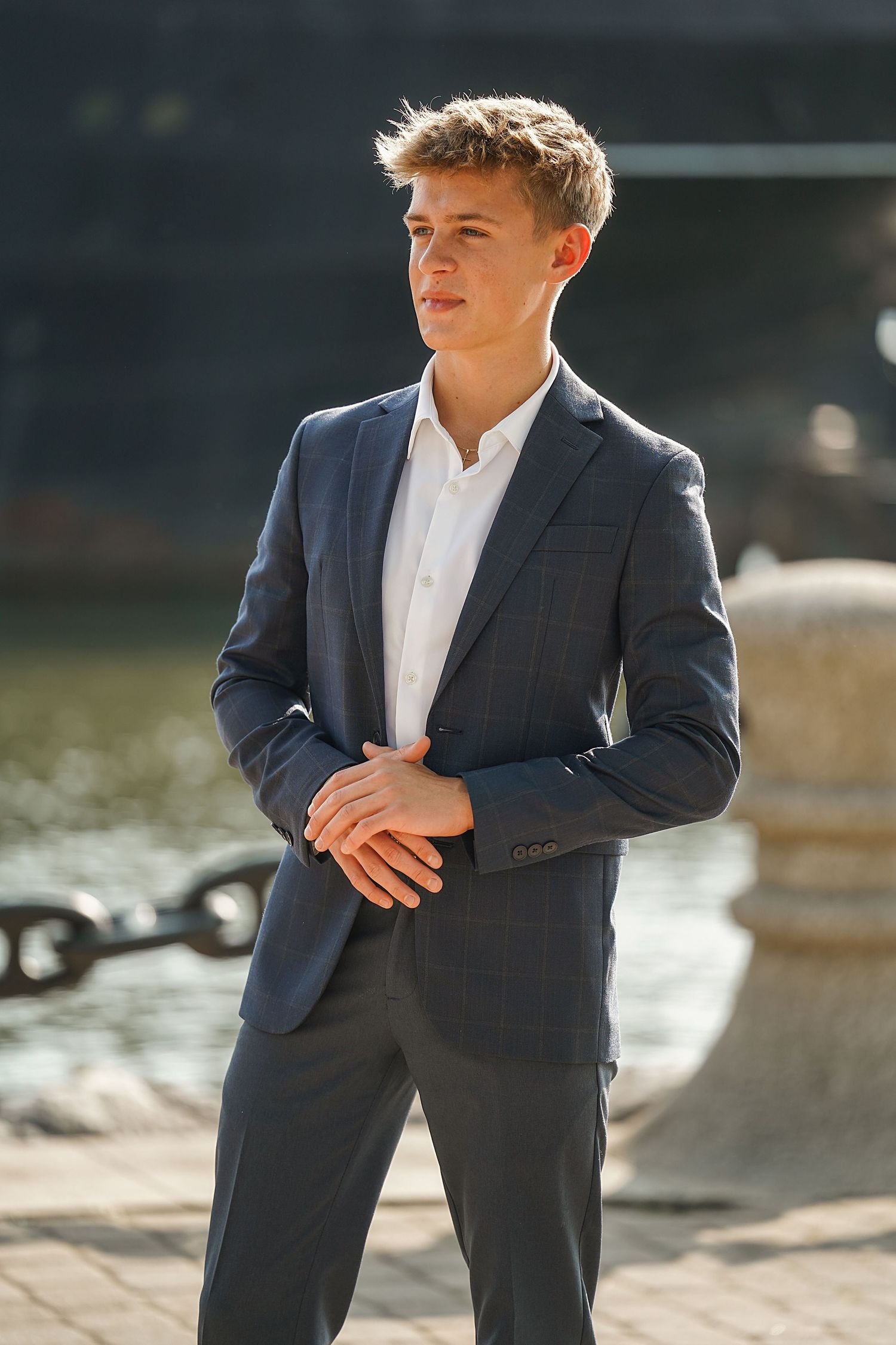 Professional portrait of a young person in a navy suit and white shirt standing outdoors in natural lighting.