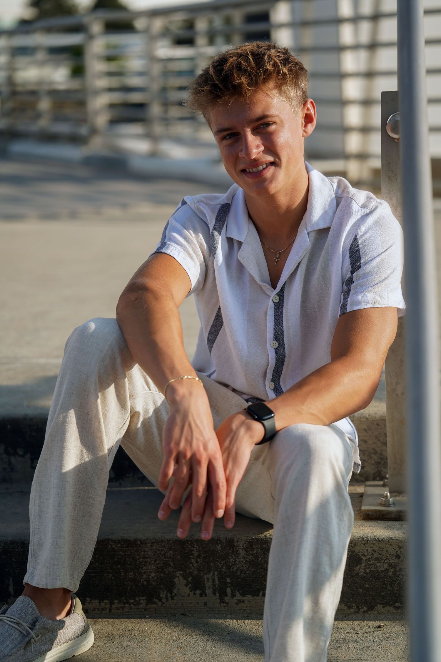Person in white button-up shirt and light pants sits casually on concrete ledge in outdoor urban setting.
