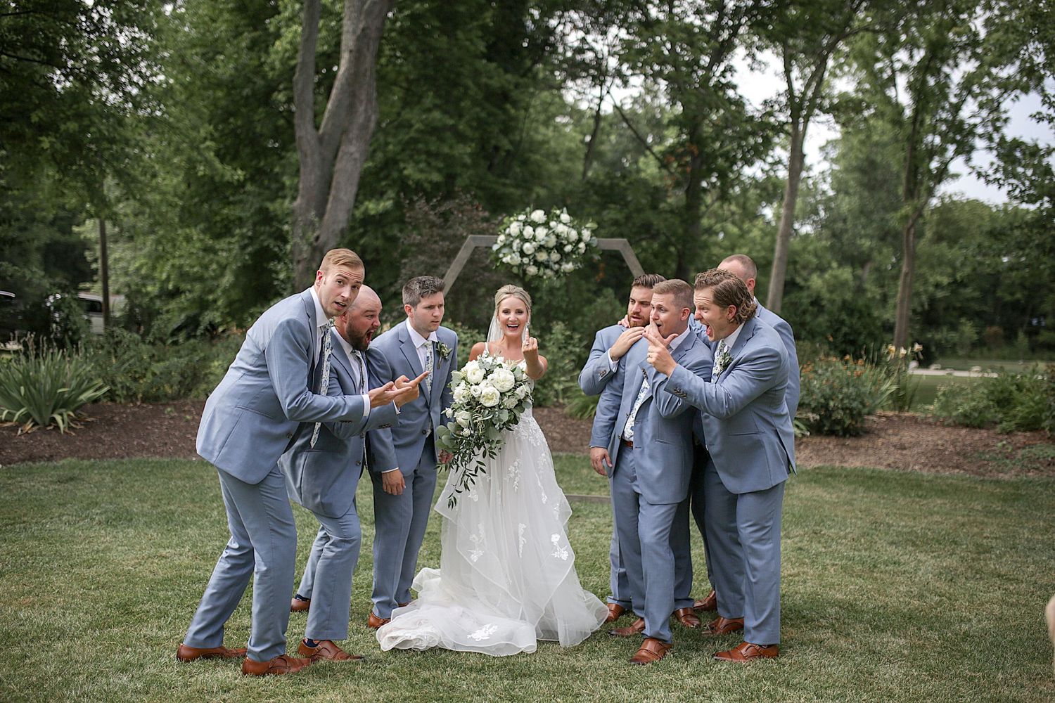 Wedding party shares candid moments and laughter on grassy lawn.