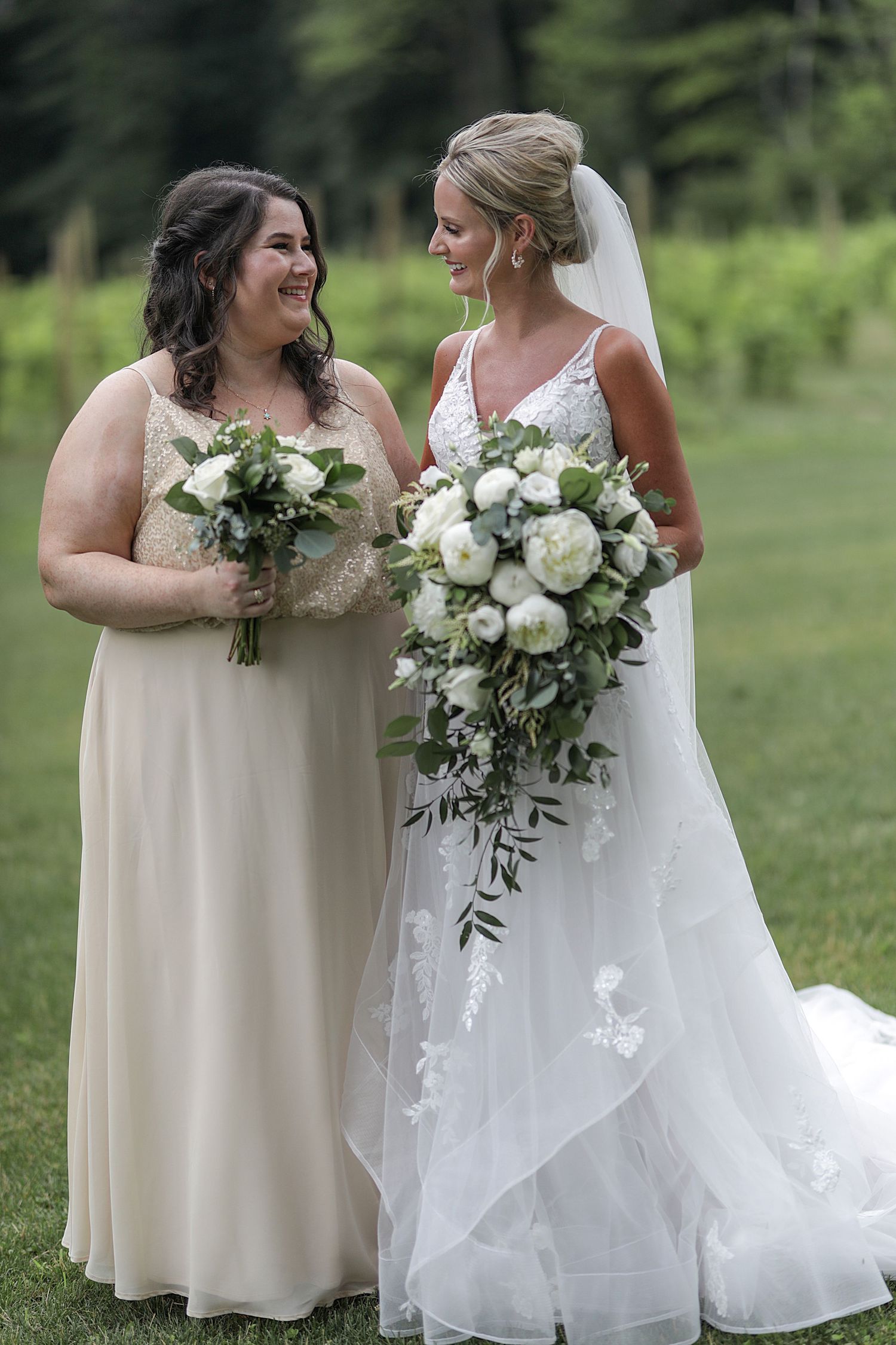 Two bridesmaids sharing a joyful moment while holding lush white bouquets outdoors.