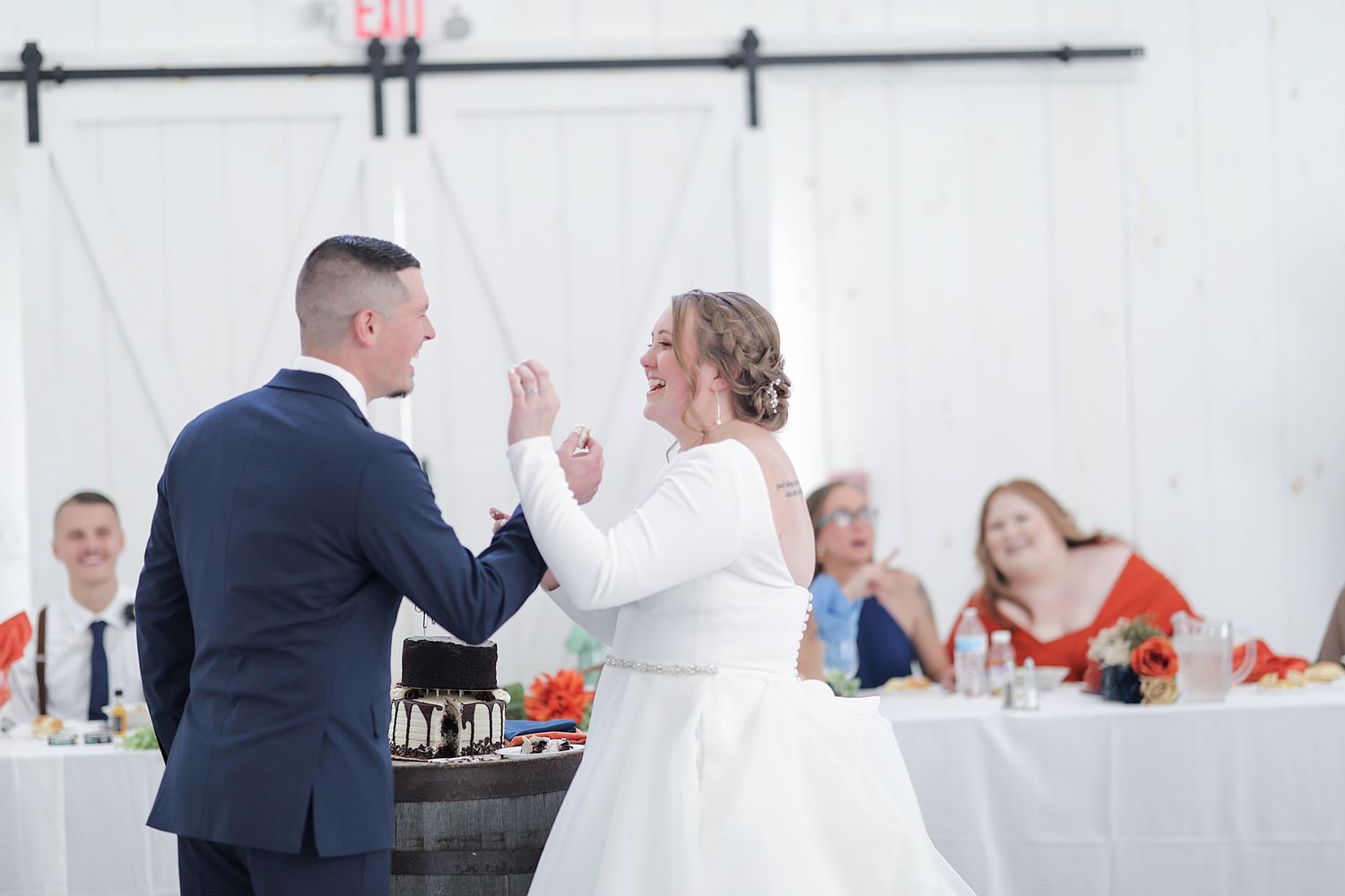 Newlyweds sharing playful moment during reception with guests in background.