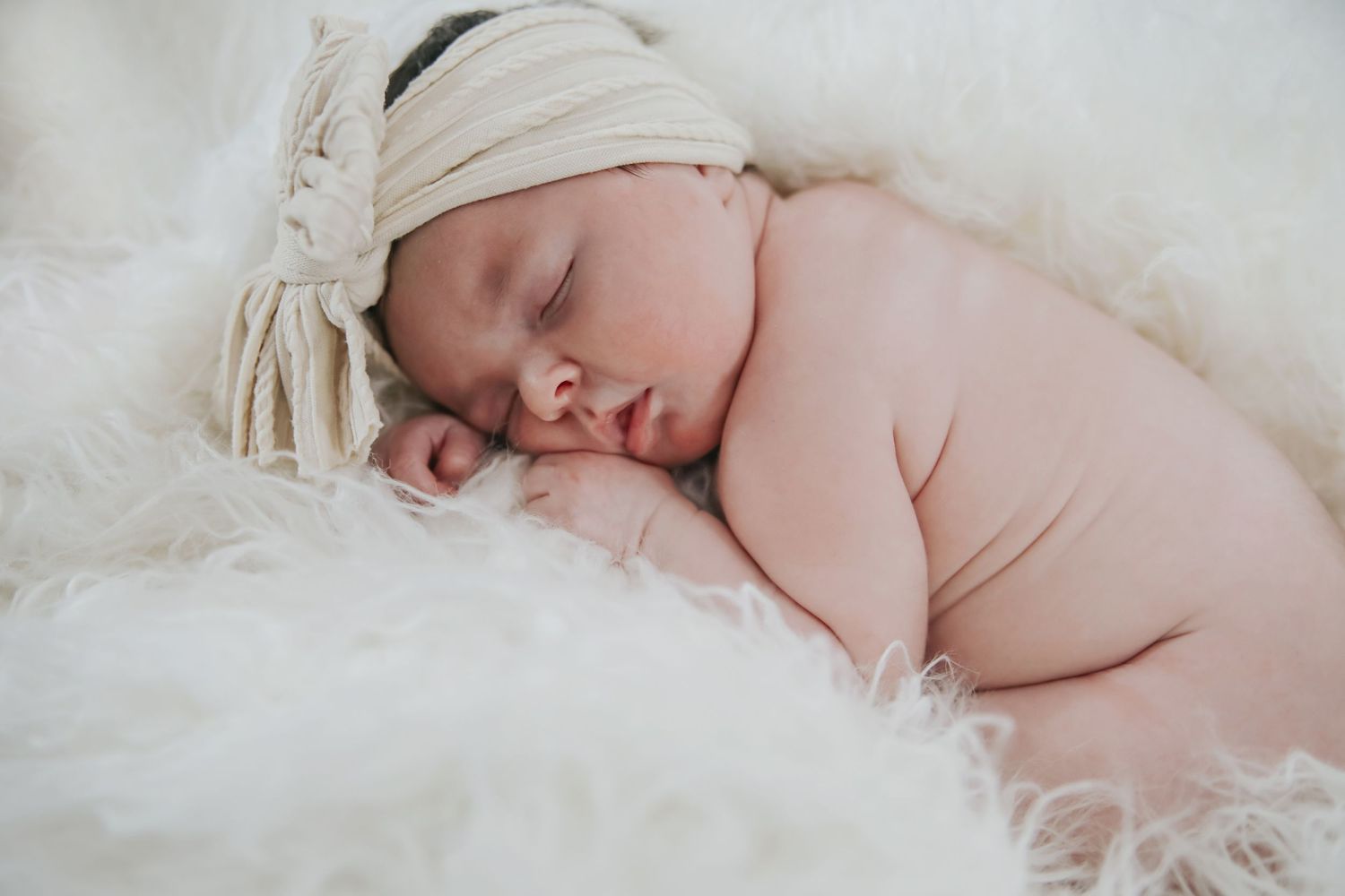 A sleeping newborn baby lies peacefully on soft white blankets in a delicate and dreamy setting.