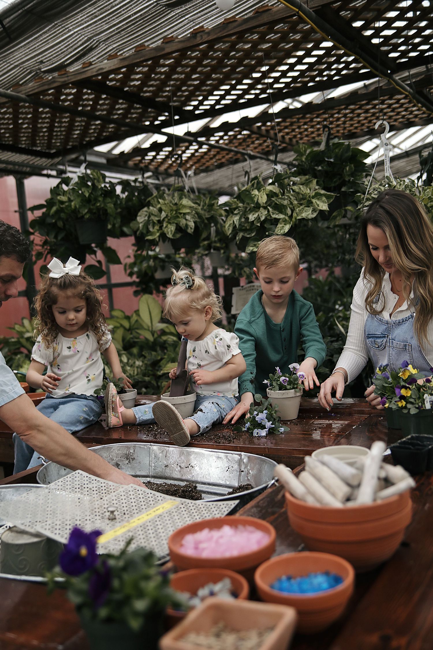 Children participate in an indoor gardening workshop with terracotta pots and planting materials under a greenhouse structure.