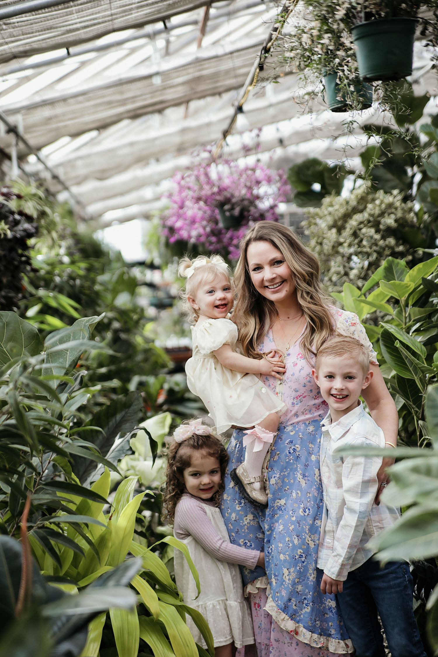 Family smiles together inside a lush greenhouse filled with tropical plants and pink flowers.