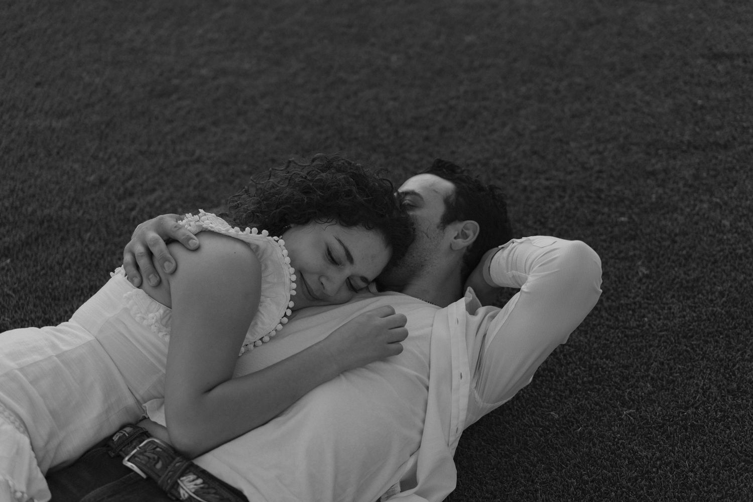 A tender black and white image of a couple lying close together while resting on grass.