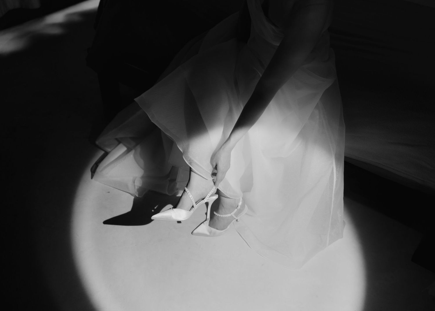 Black and white photo of elegant white stiletto heels beside dark shoes under flowing fabric.