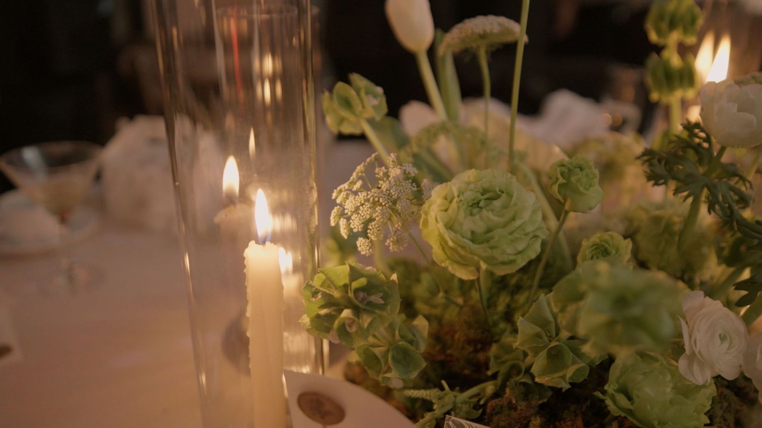 Elegant wedding reception table setting with candlelight, white flowers and greenery decorations in romantic ambiance.