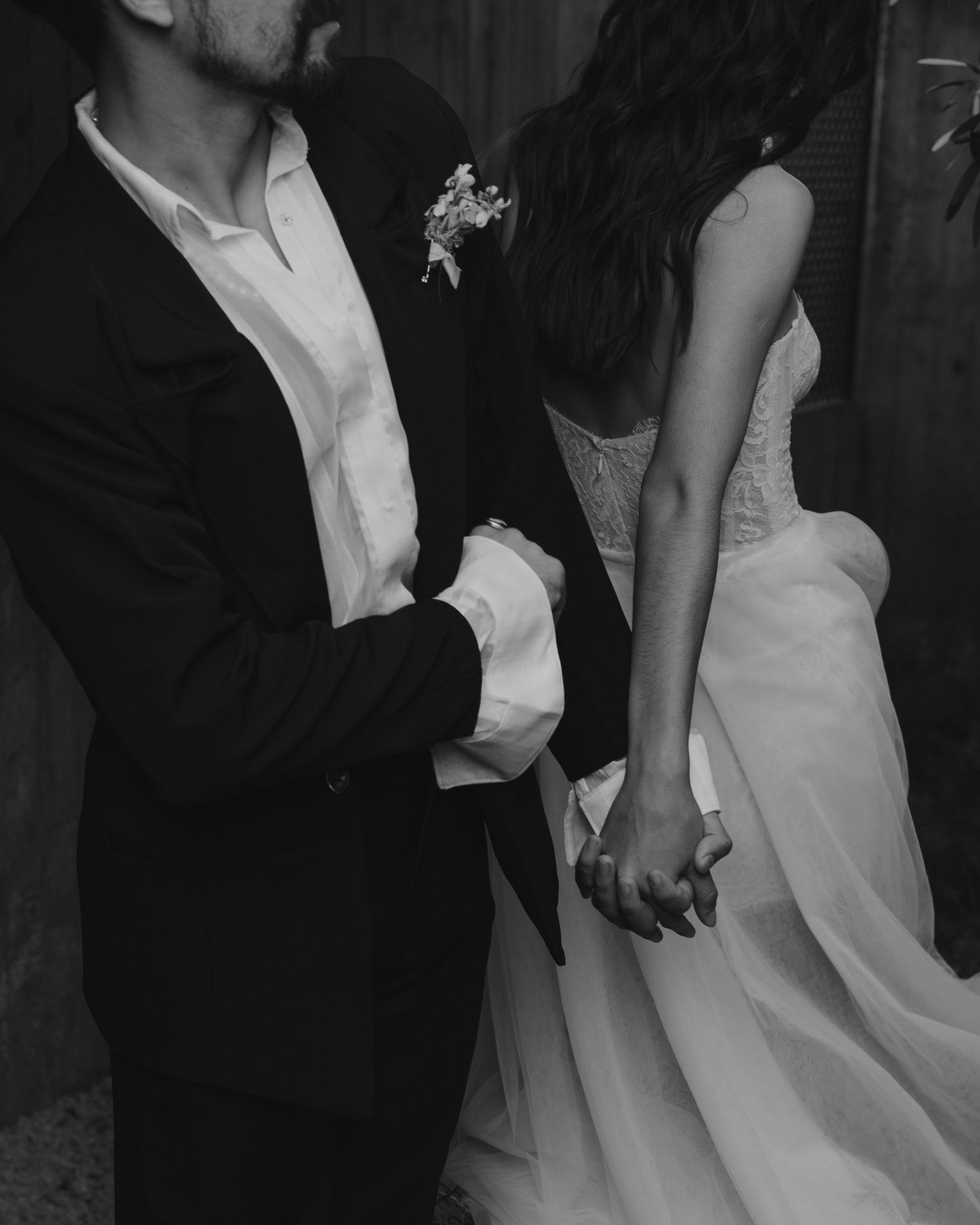 Artistic black and white capture of a couple's formal wedding attire and clasped hands.