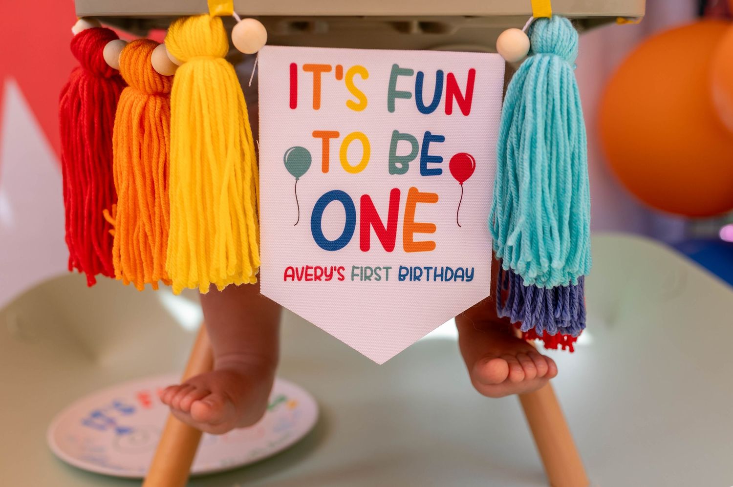 Colorful first birthday banner reading It's Fun To Be One with rainbow tassels for Avedy's first birthday party.