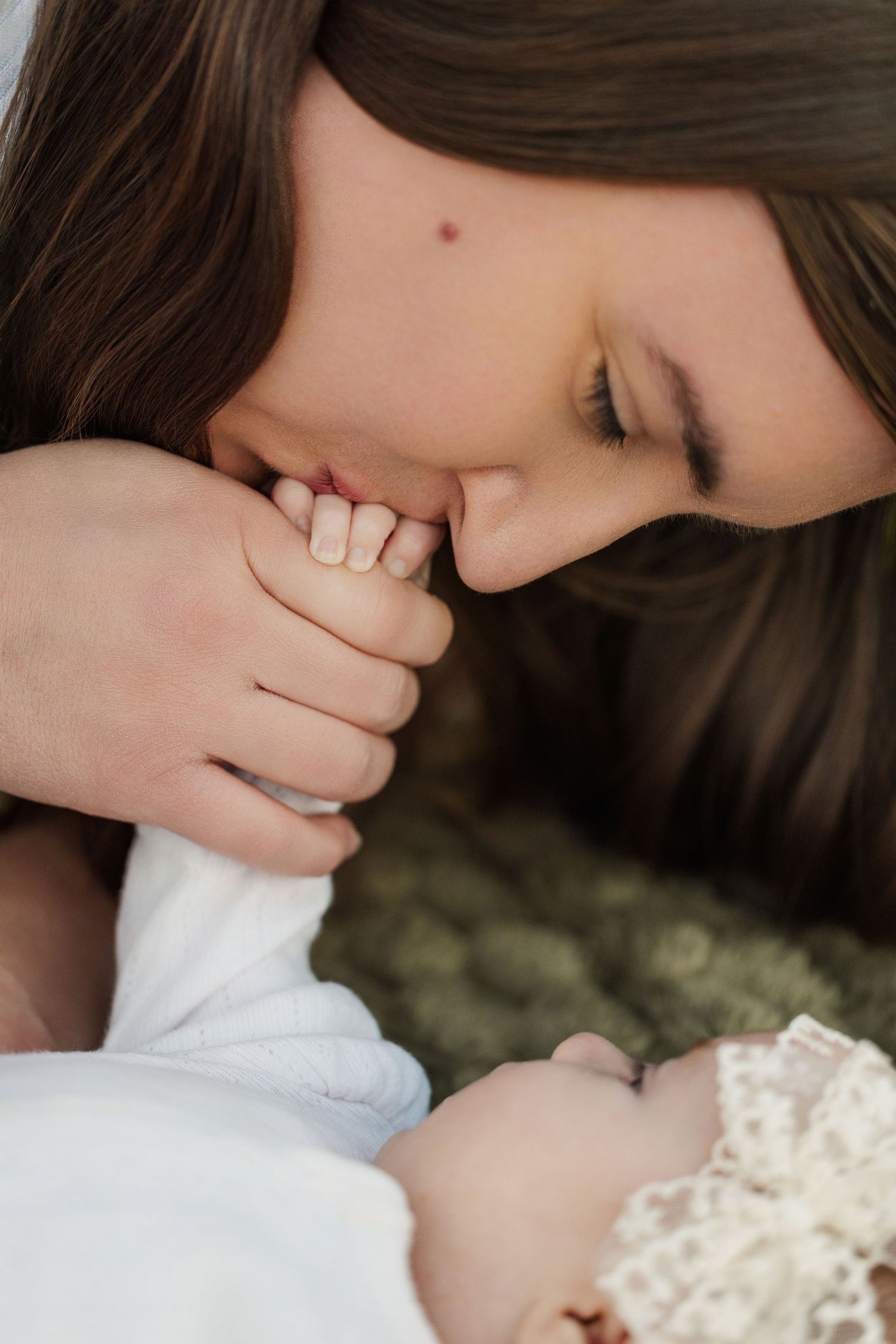 A tender mother gently kisses her newborn baby's tiny hand in a soft, intimate close-up portrait.