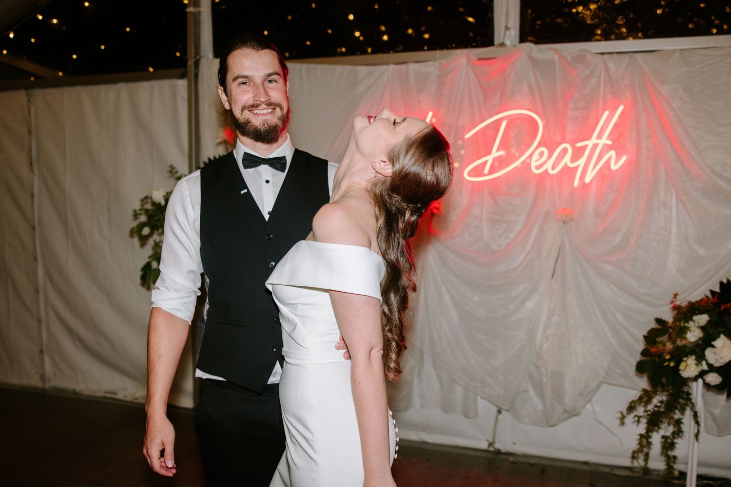 A romantic wedding celebration at night with a neon sign glowing in pink against a white backdrop.