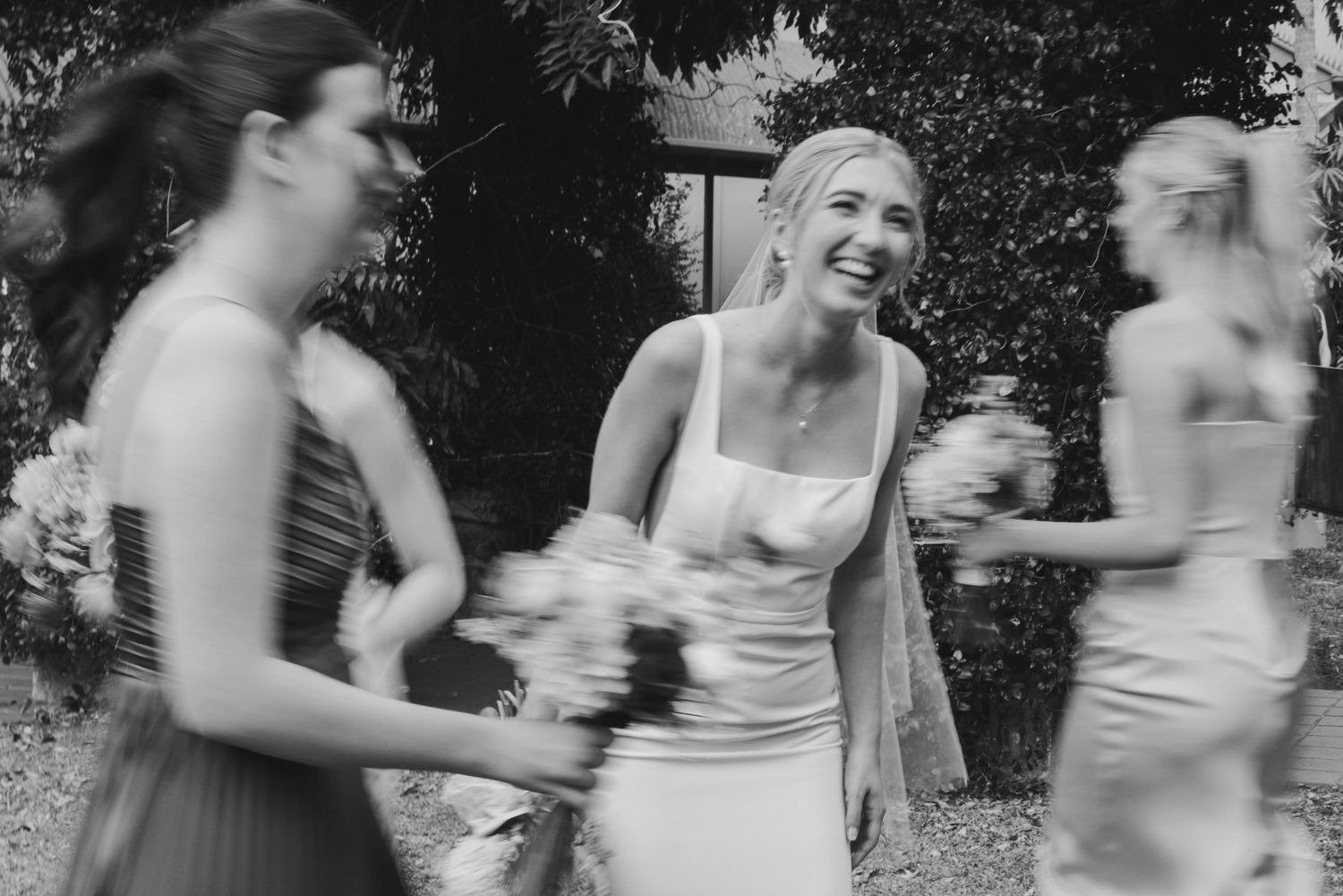 A group of bridesmaids in white dresses dance and laugh together during a wedding celebration.