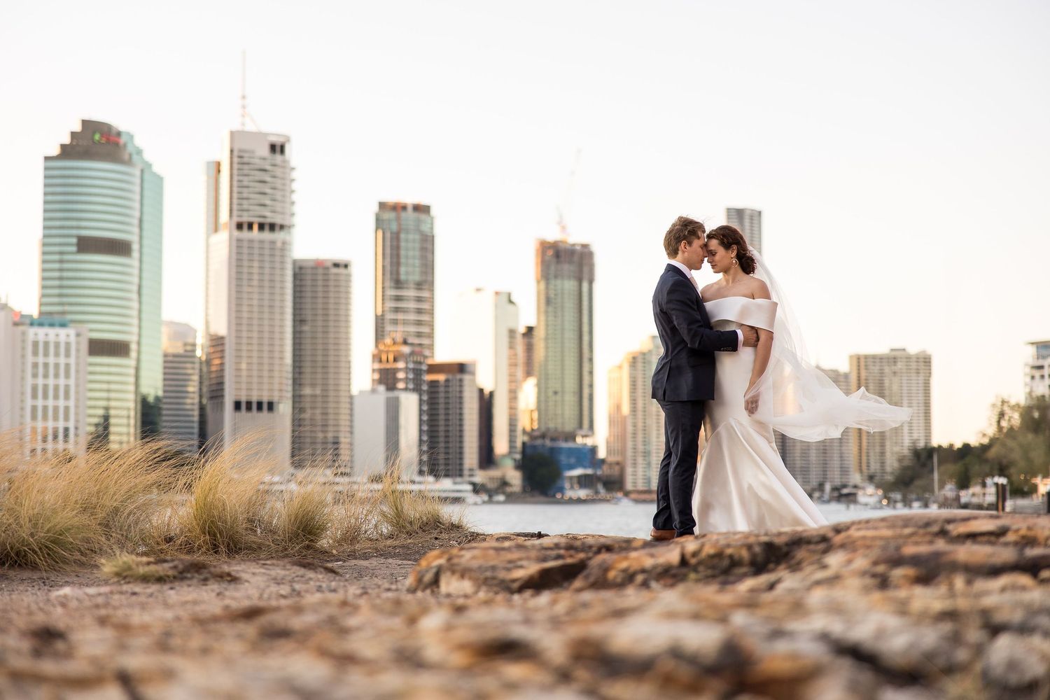 A romantic couple shares a tender moment against the Brisbane city skyline during golden hour.