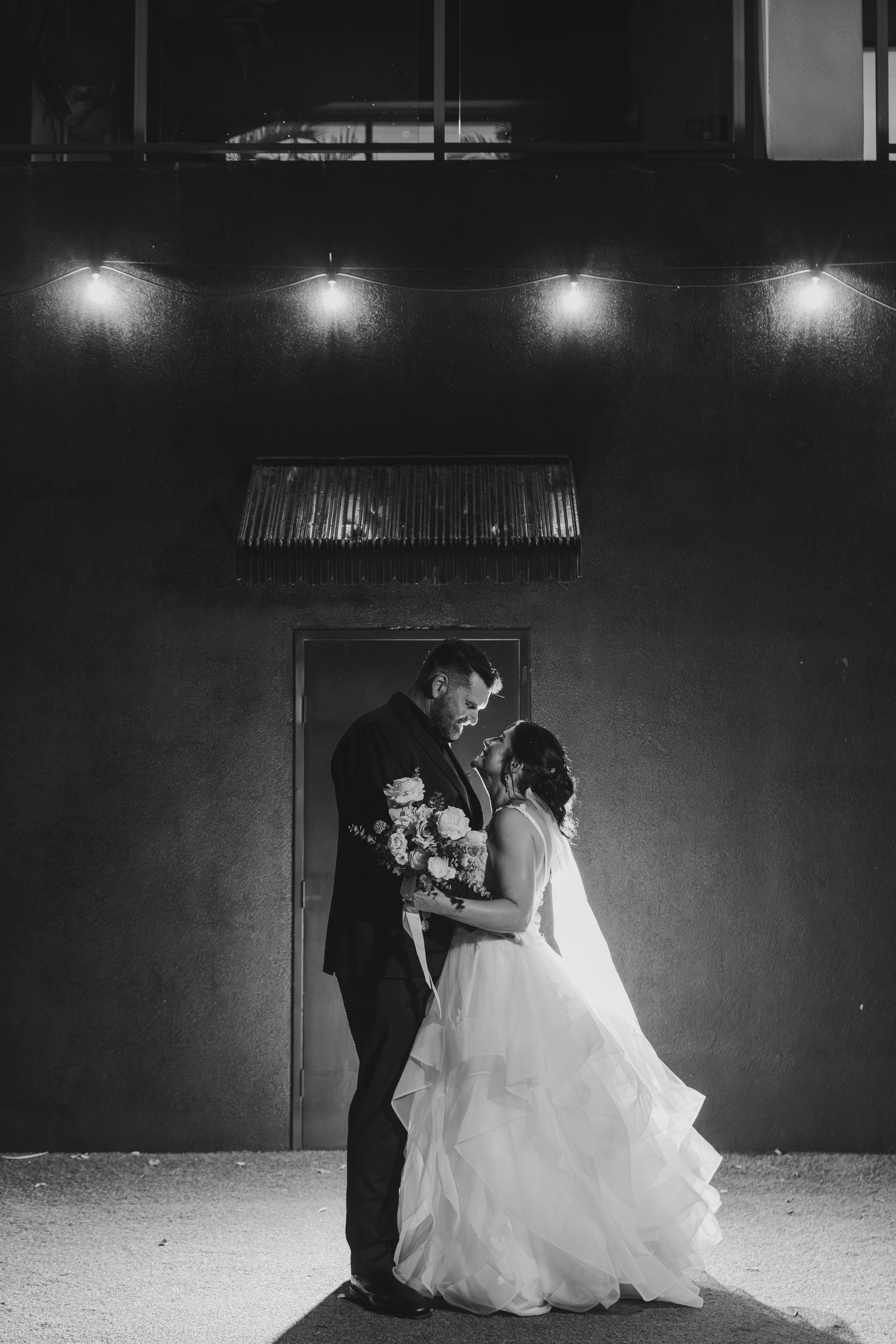 A romantic black and white wedding photo series showing a couple dancing under outdoor lights at night.