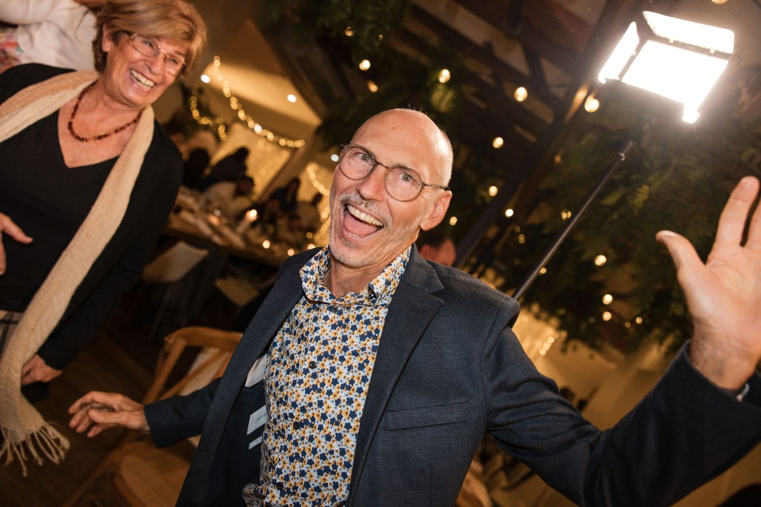 Joyful bald man in floral shirt and blazer laughing at a festive indoor party event.