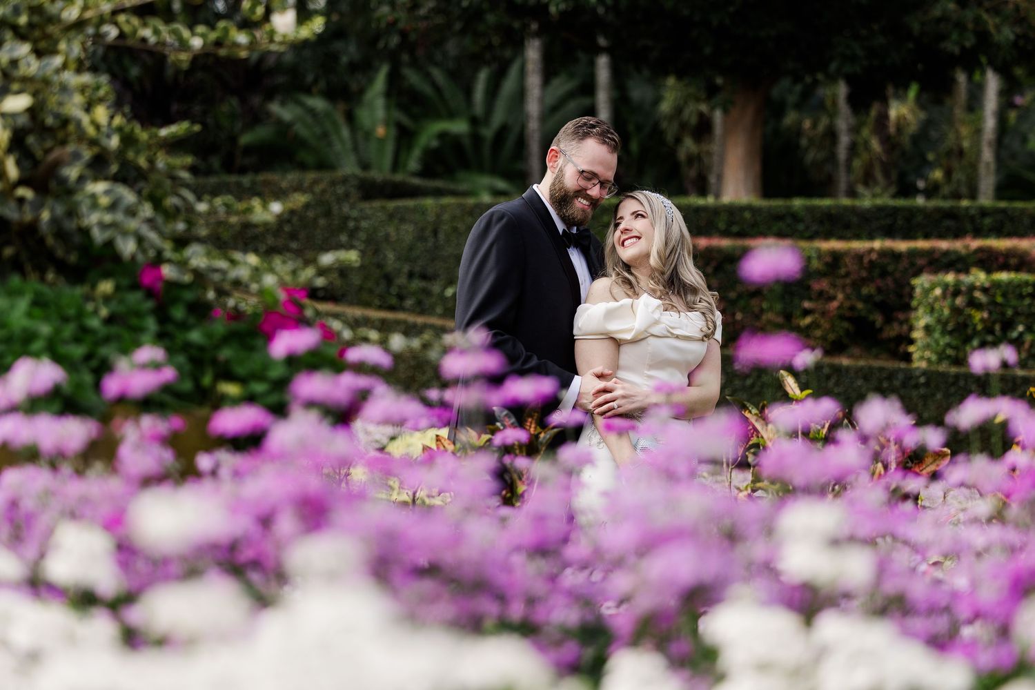 Pink cosmos flowers bloom in a lush garden setting with trees and natural landscaping in the background.