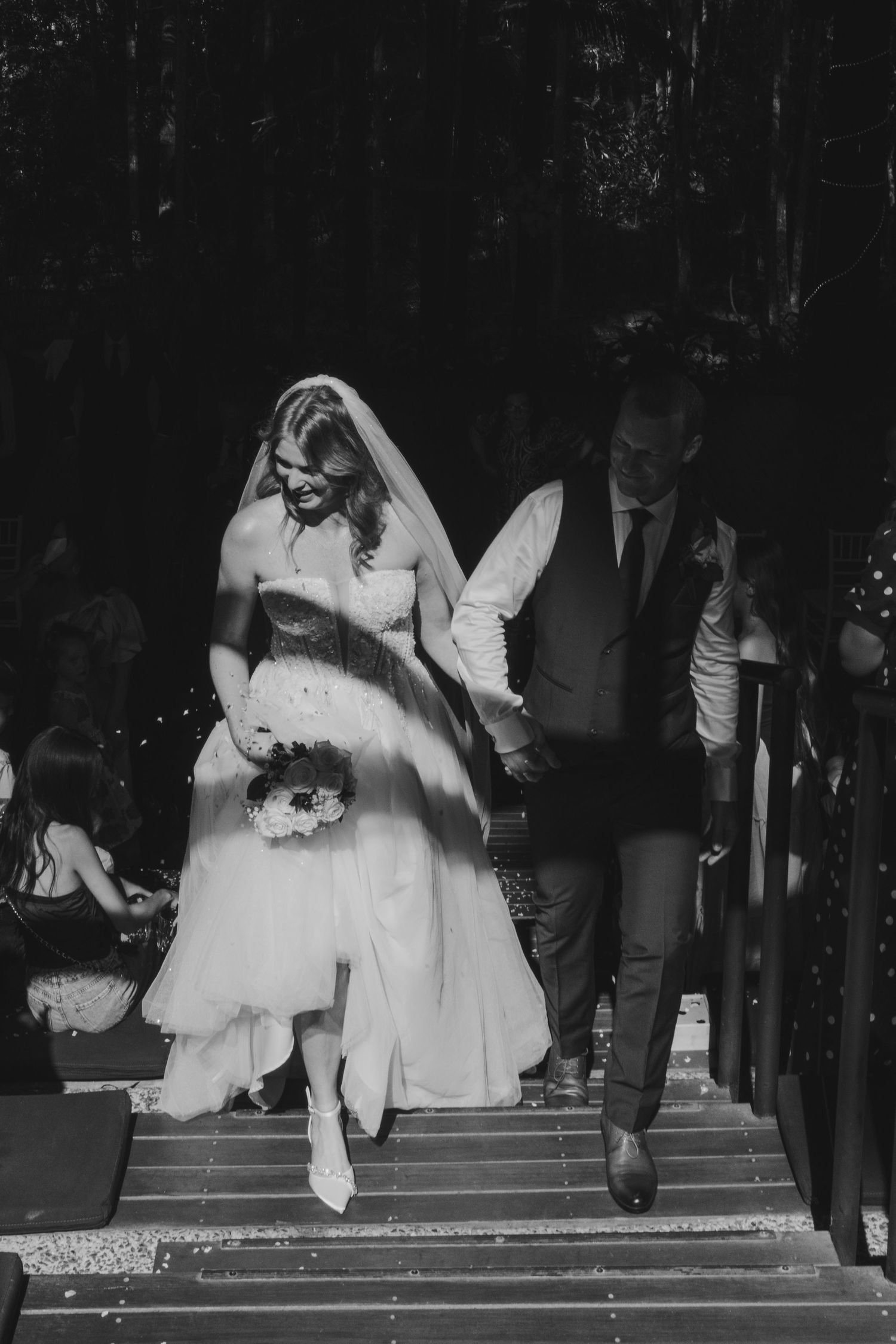 Black and white wedding photos show a bride's dress flowing dramatically as she descends steps with guests looking on.