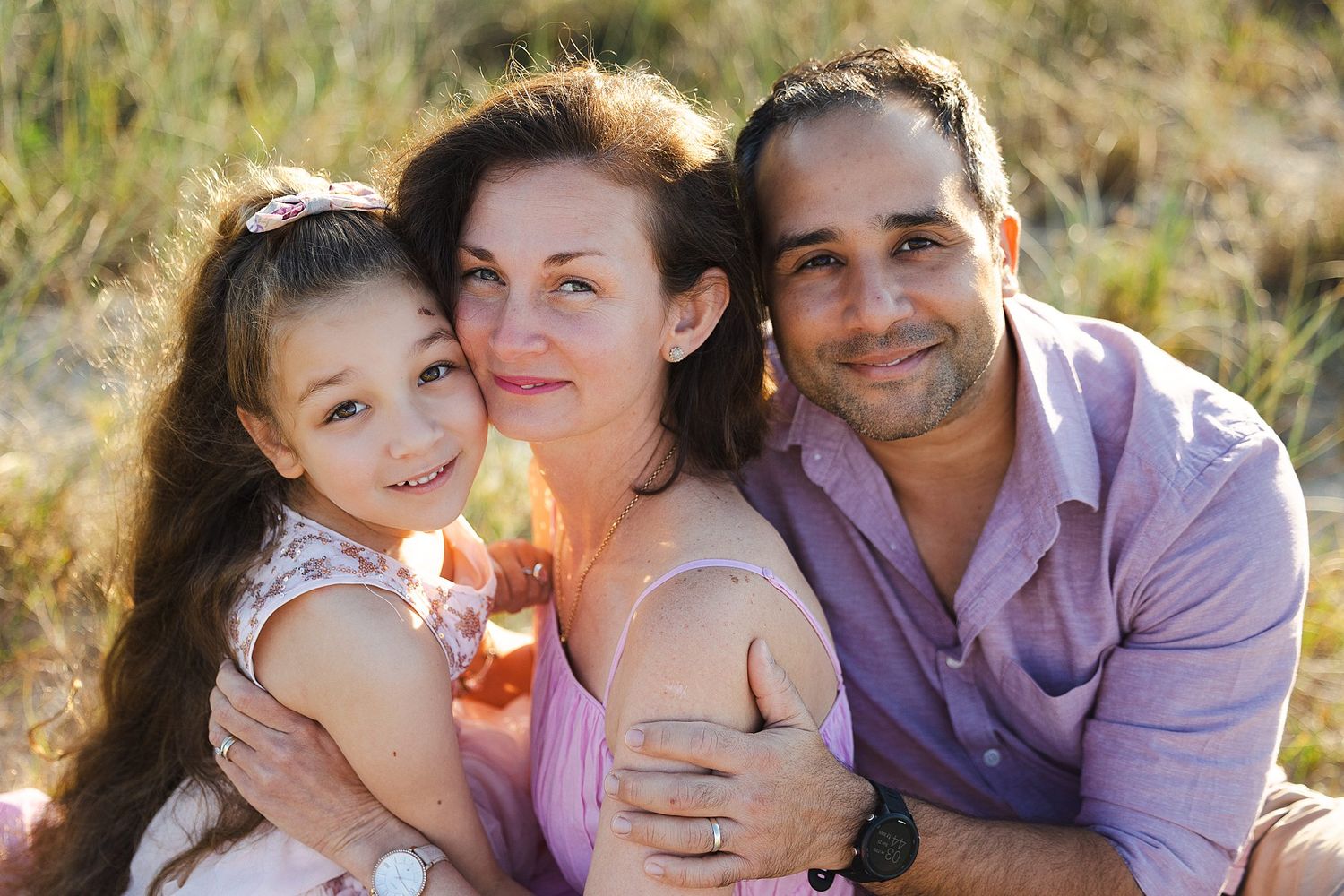 A happy family poses together outdoors in warm sunlight during a relaxed photo session in nature.