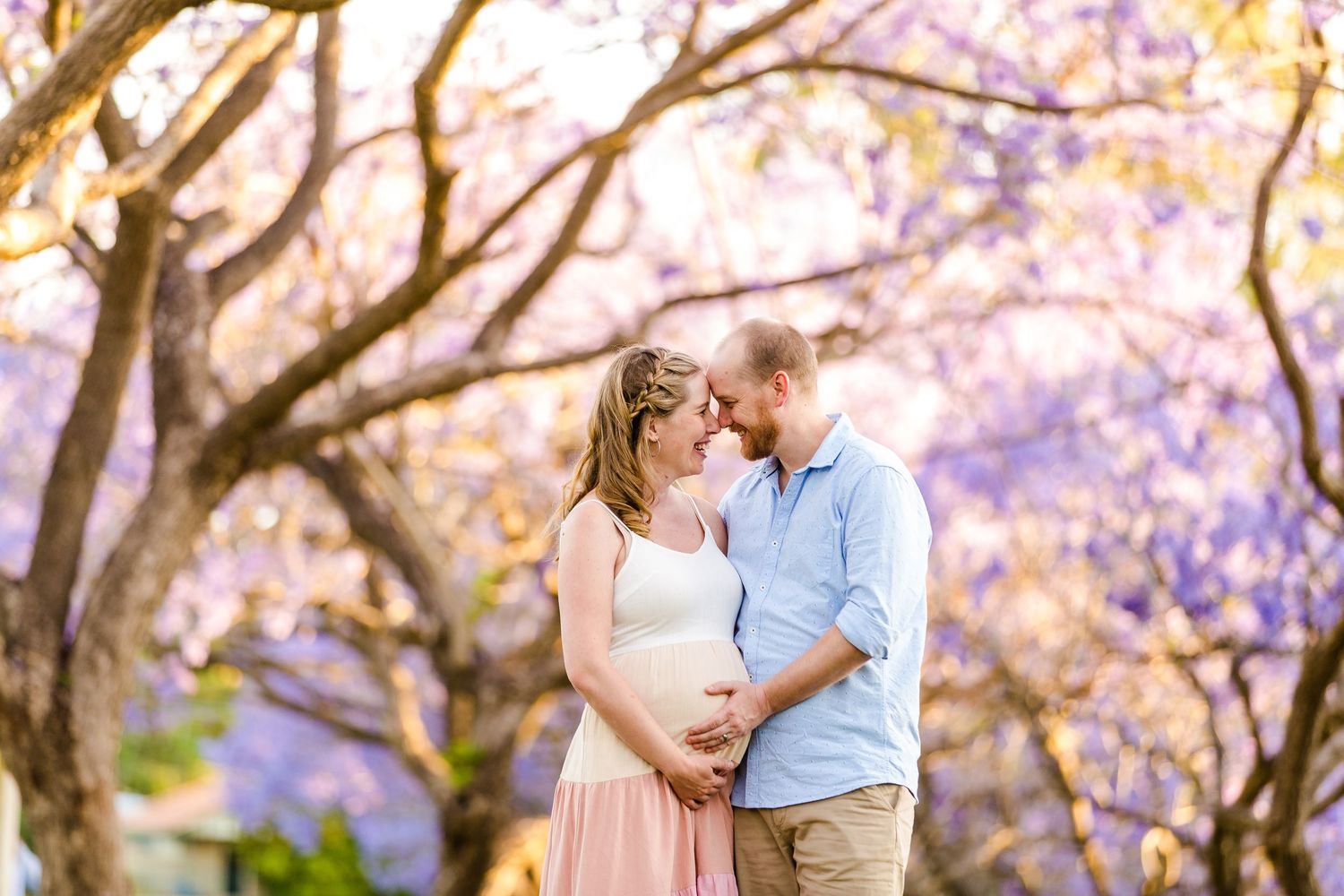 A romantic couple embraces under beautiful blooming jacaranda trees with purple flowers in a dreamy outdoor setting.