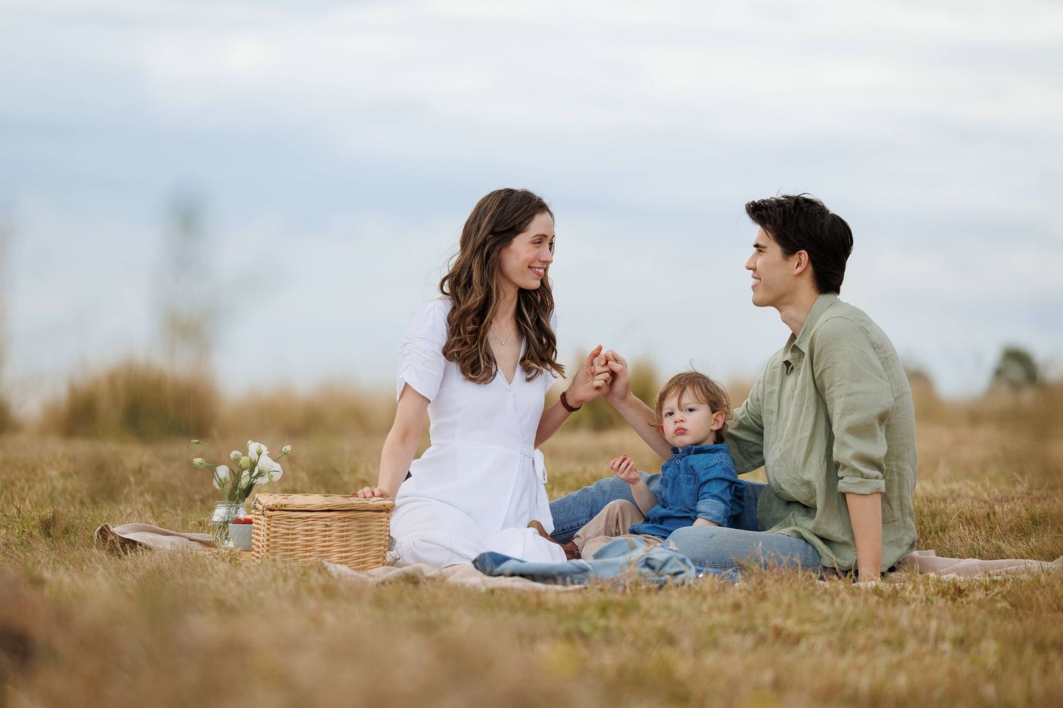 Family enjoys a peaceful picnic together on a blanket in a rustic outdoor field setting.