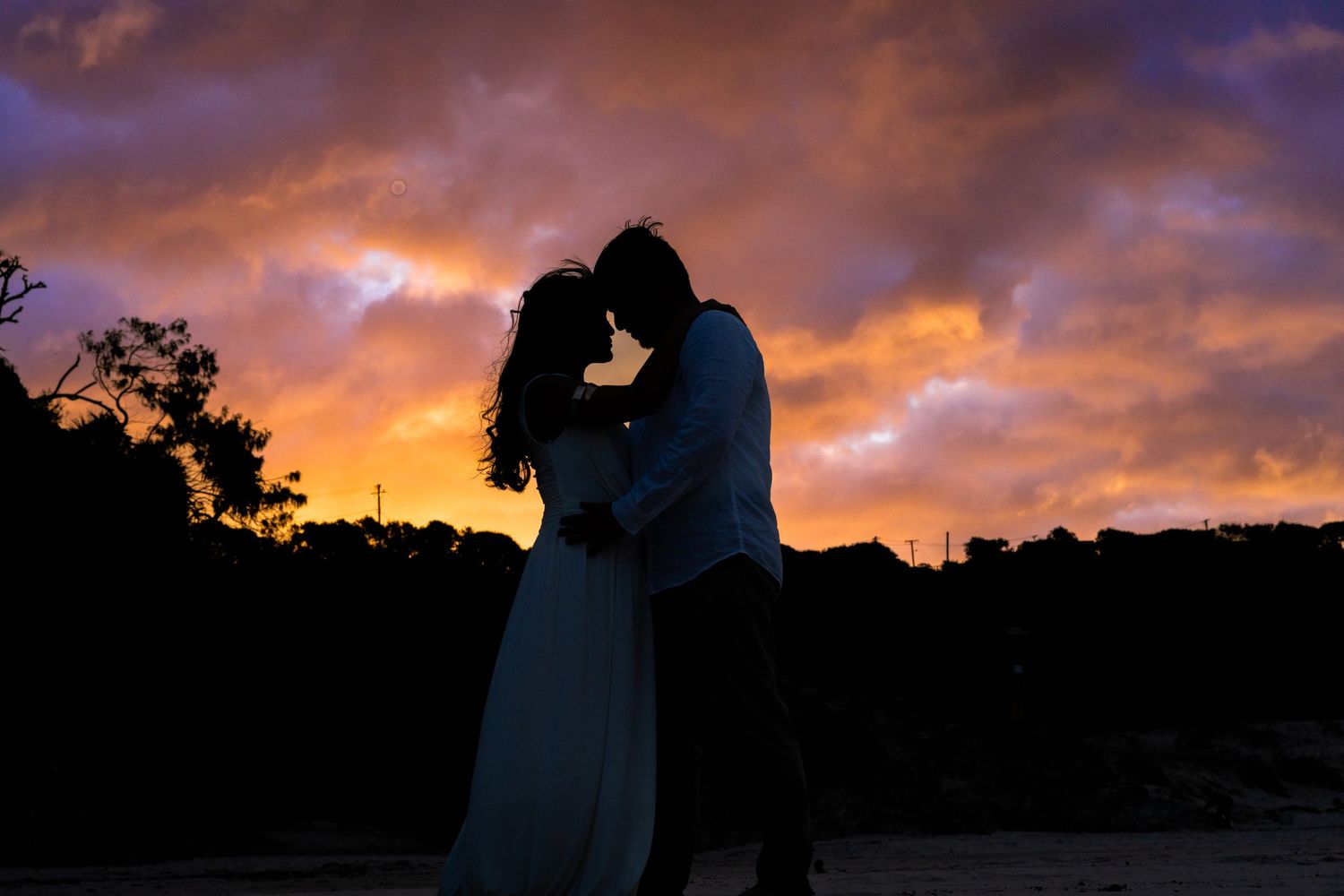 Silhouette of a romantic couple embracing at sunset with dramatic purple and orange clouds in the background.