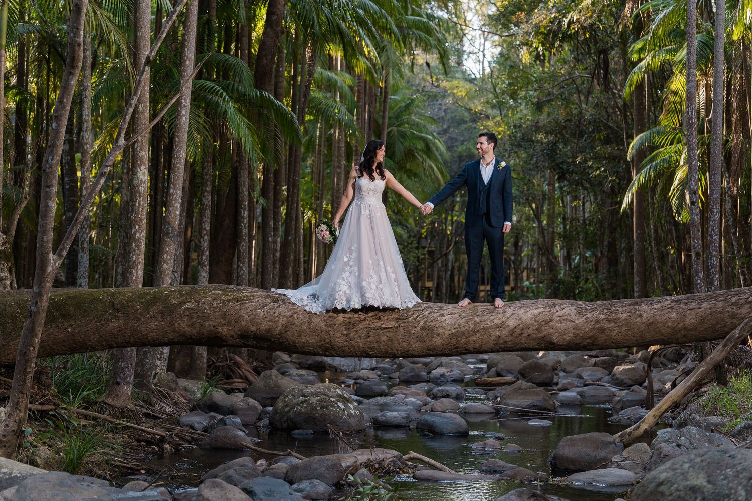 A wedding photoshoot on a rustic stone path surrounded by tropical palm trees and natural landscaping.