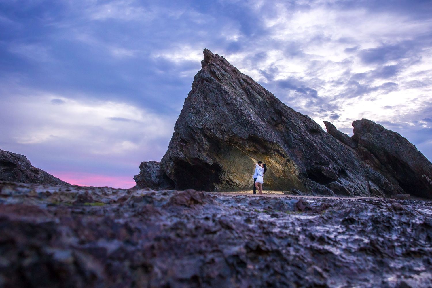 Silhouetted figure stands at dramatic rocky outcrop against purple sunset sky.