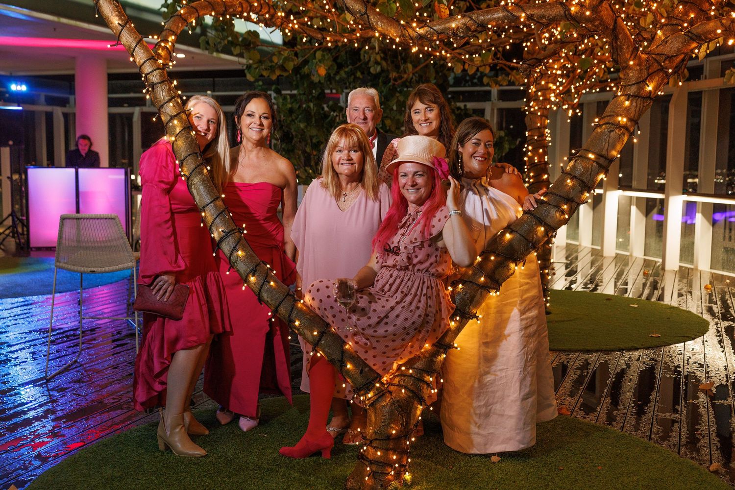 A group poses together at a party venue decorated with illuminated heart-shaped lights and holiday decorations.