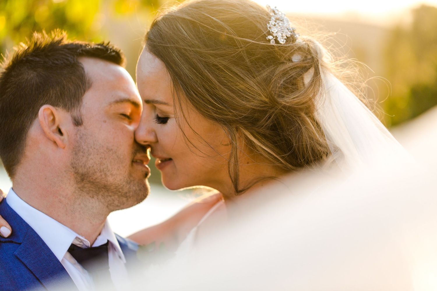 A tender wedding moment captured in golden sunlight with a flowing veil.