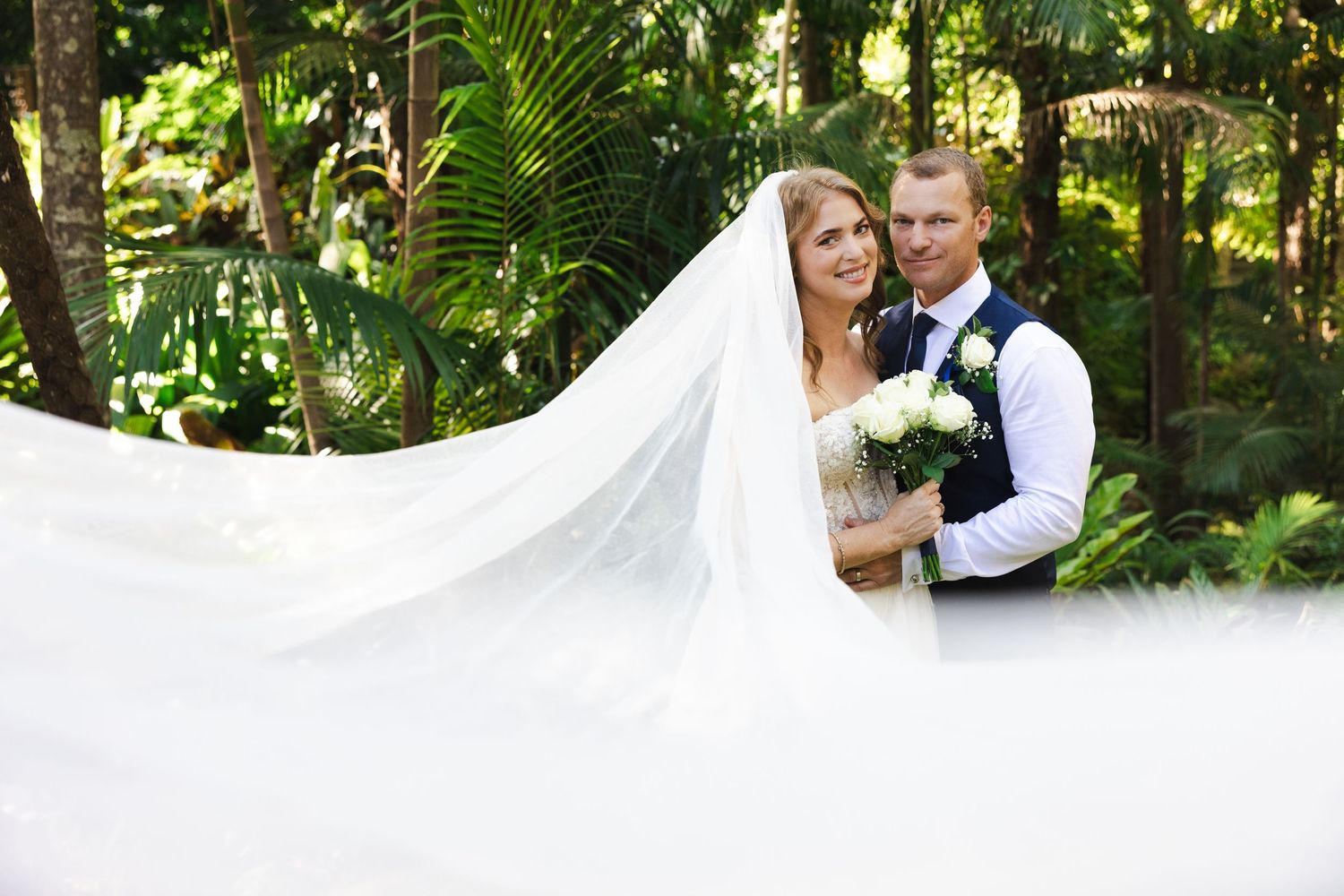 A wedding couple poses together in a lush garden setting during their outdoor celebration.