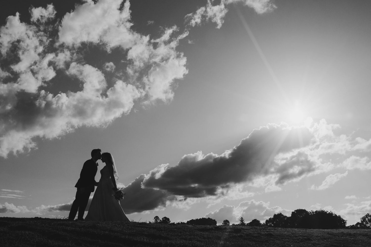 A black and white panoramic sequence of silhouettes against dramatic cloudy skies during sunset.