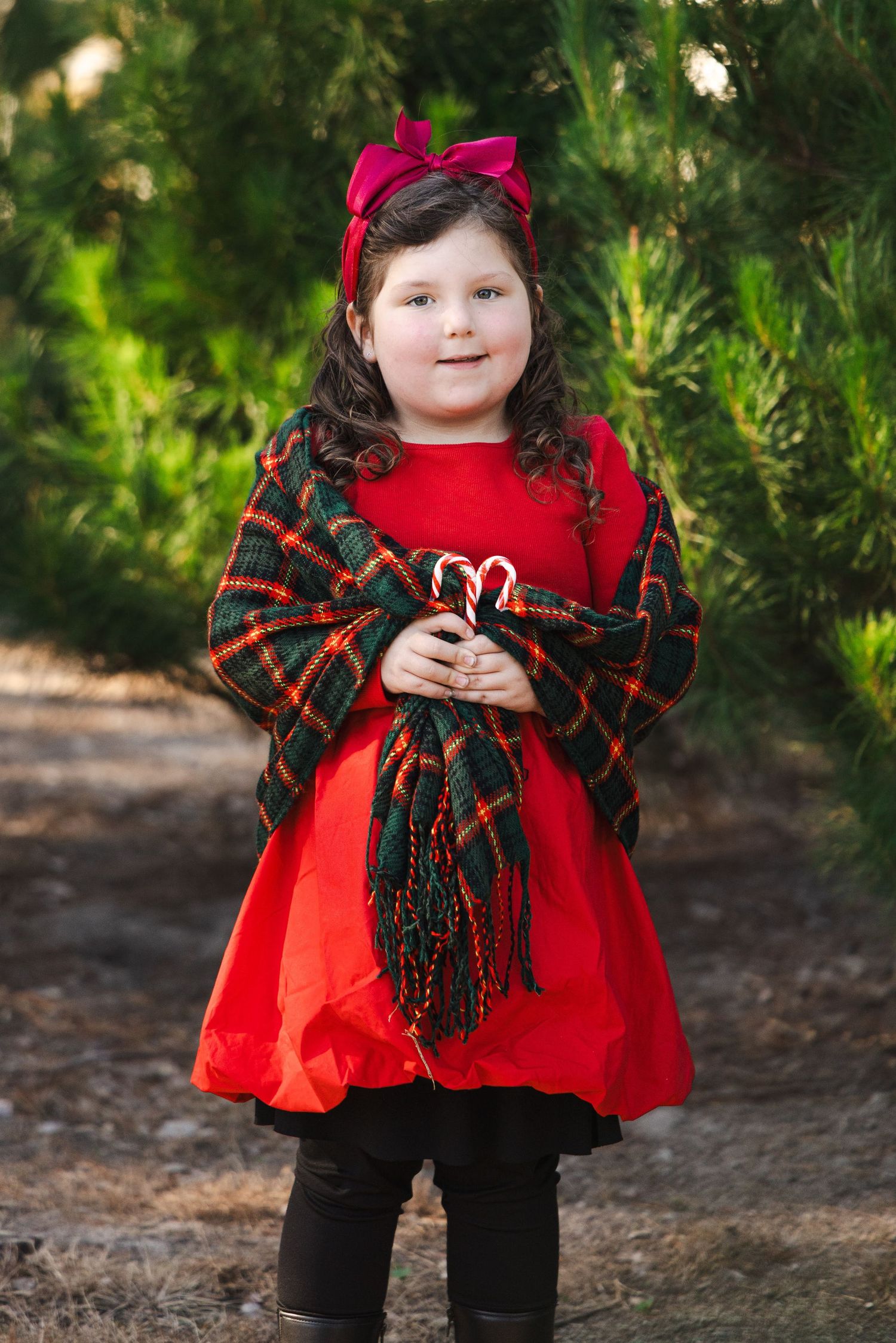 A small figure in a red dress and plaid shawl poses in front of greenery in a series of outdoor portraits.