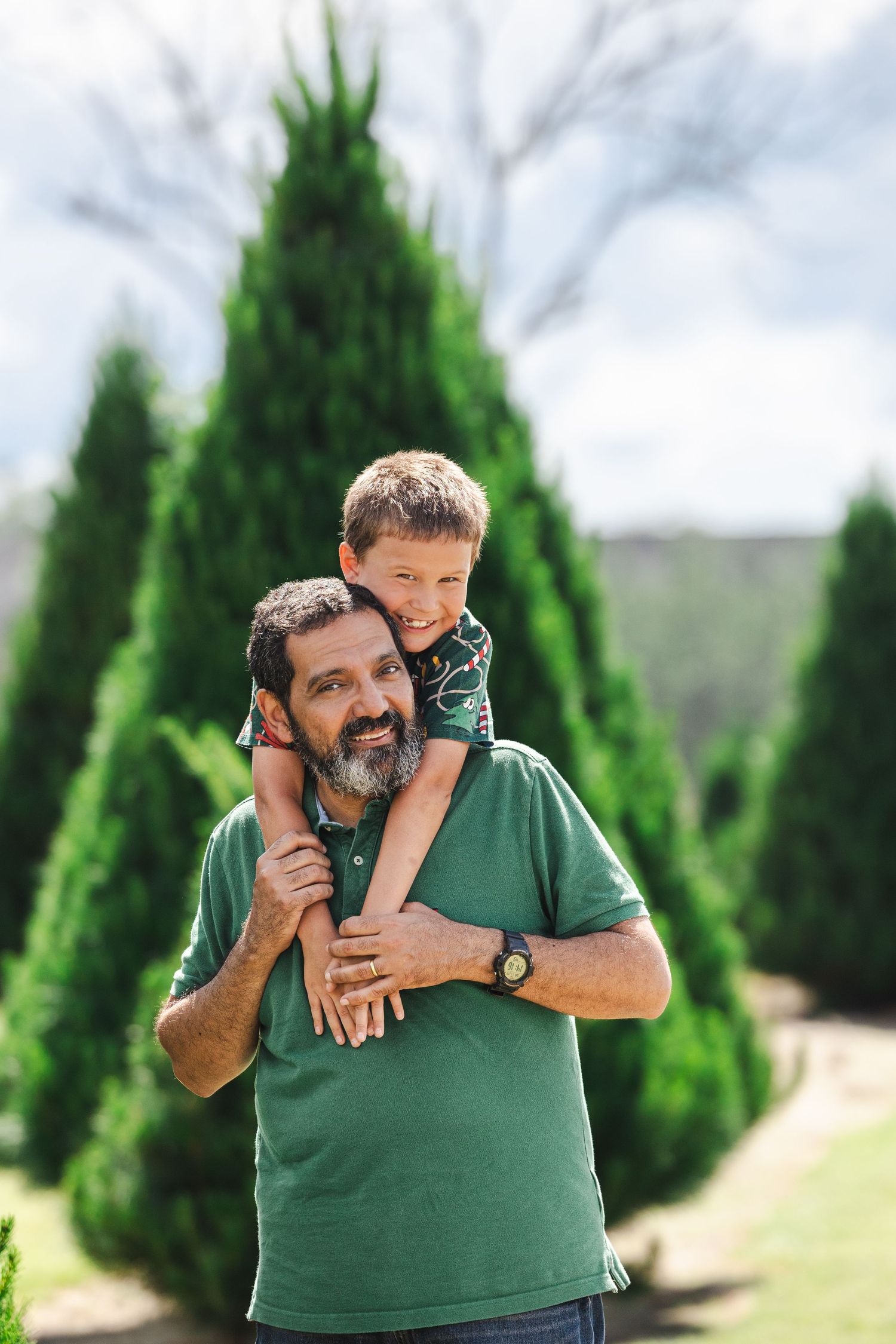 A playful moment outdoors with evergreen trees in the background as someone carries a child on their shoulders.