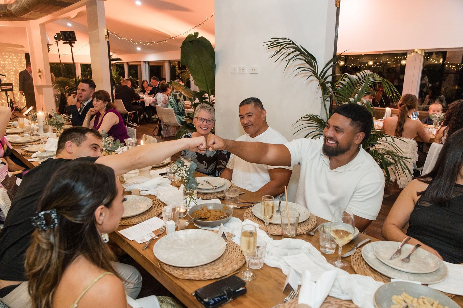 Friends toasting at a festive restaurant dinner table with elegant place settings and tropical decor.