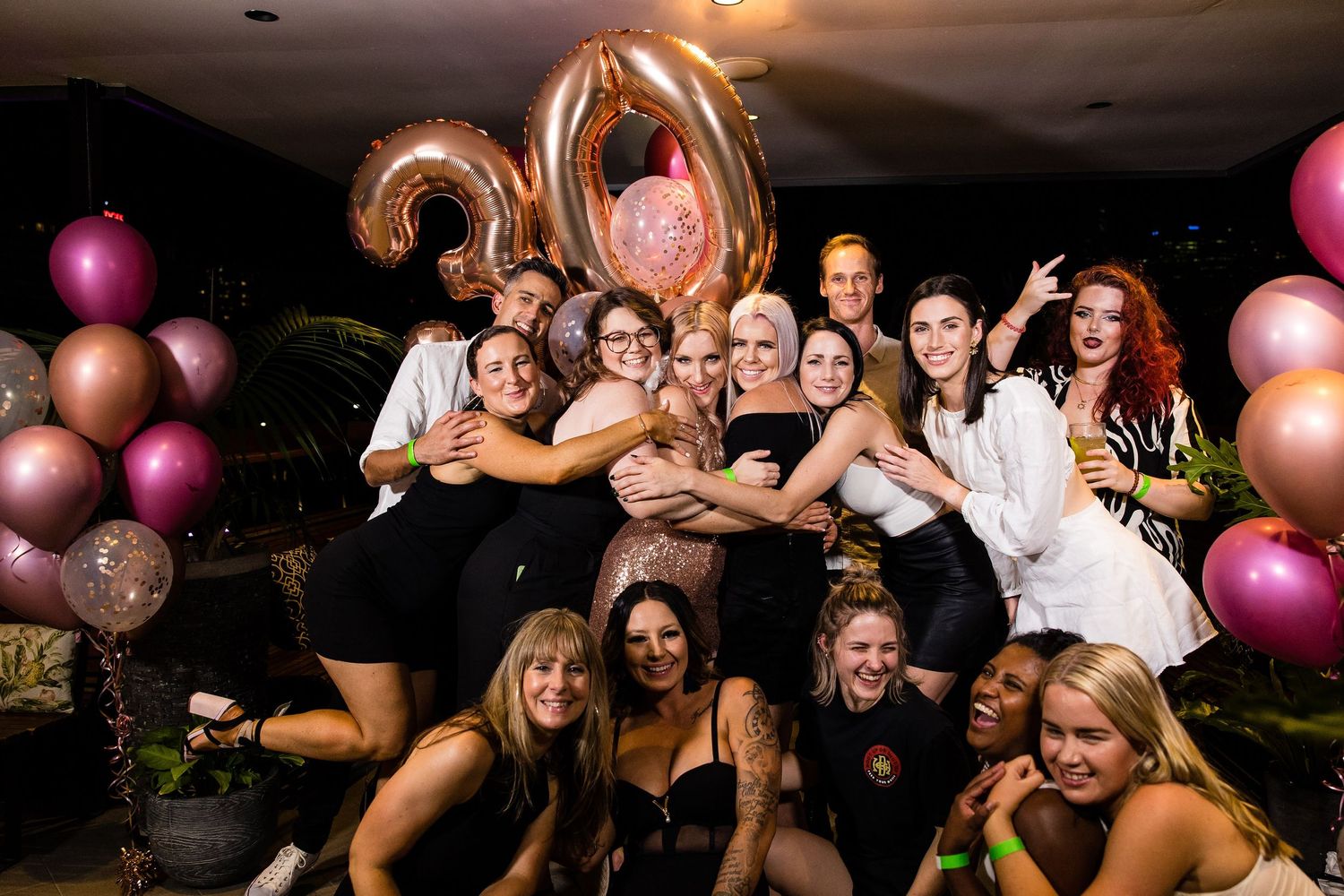 Group celebrating at a party with pink and gold balloons in a dark room.