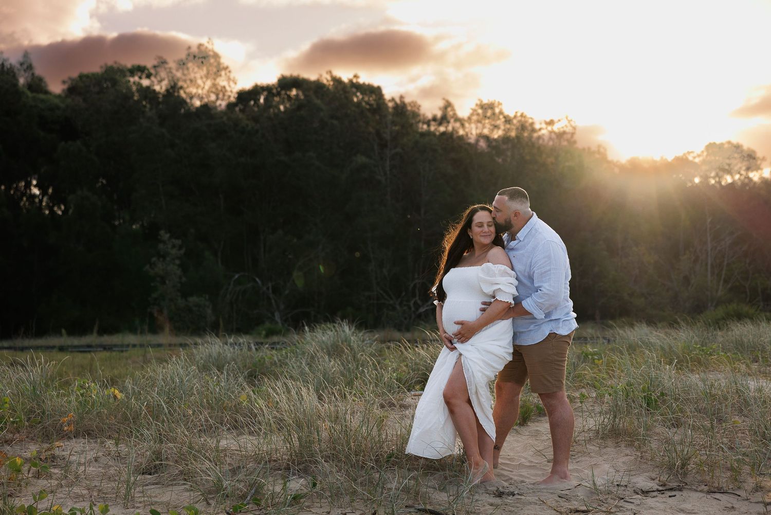 A couple shares an intimate embrace in a field at sunset during a romantic photoshoot.