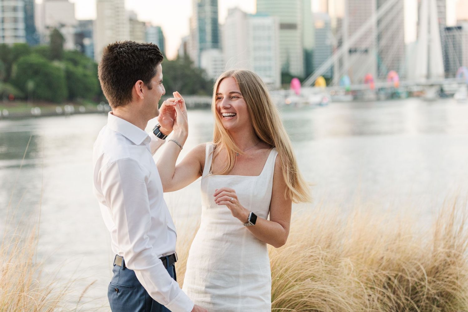 A couple in white outfits dances and laughs together in a romantic outdoor photoshoot at sunset.
