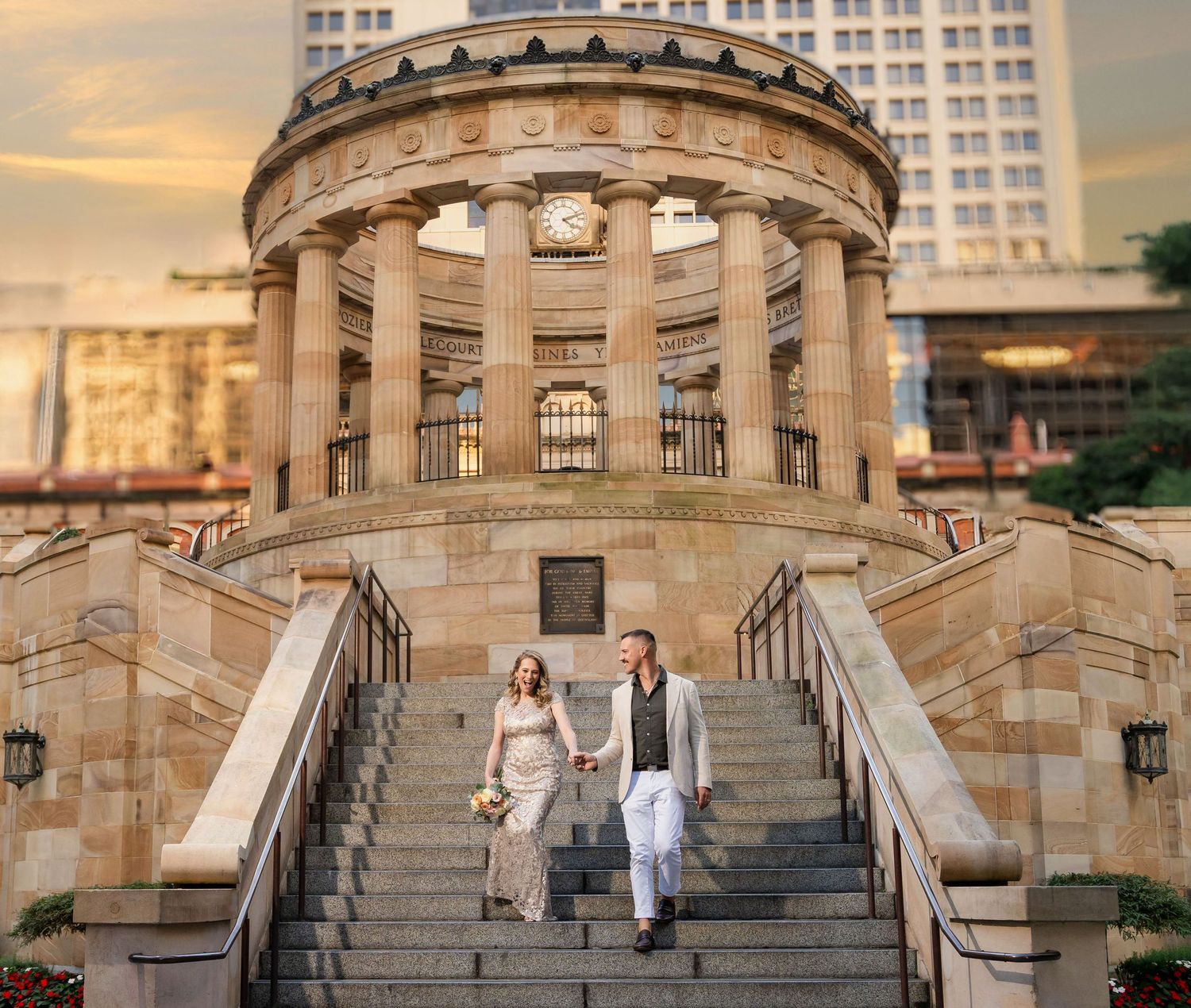 Elegant stone rotunda with classical columns and grand staircase at sunset, with a couple descending the steps.