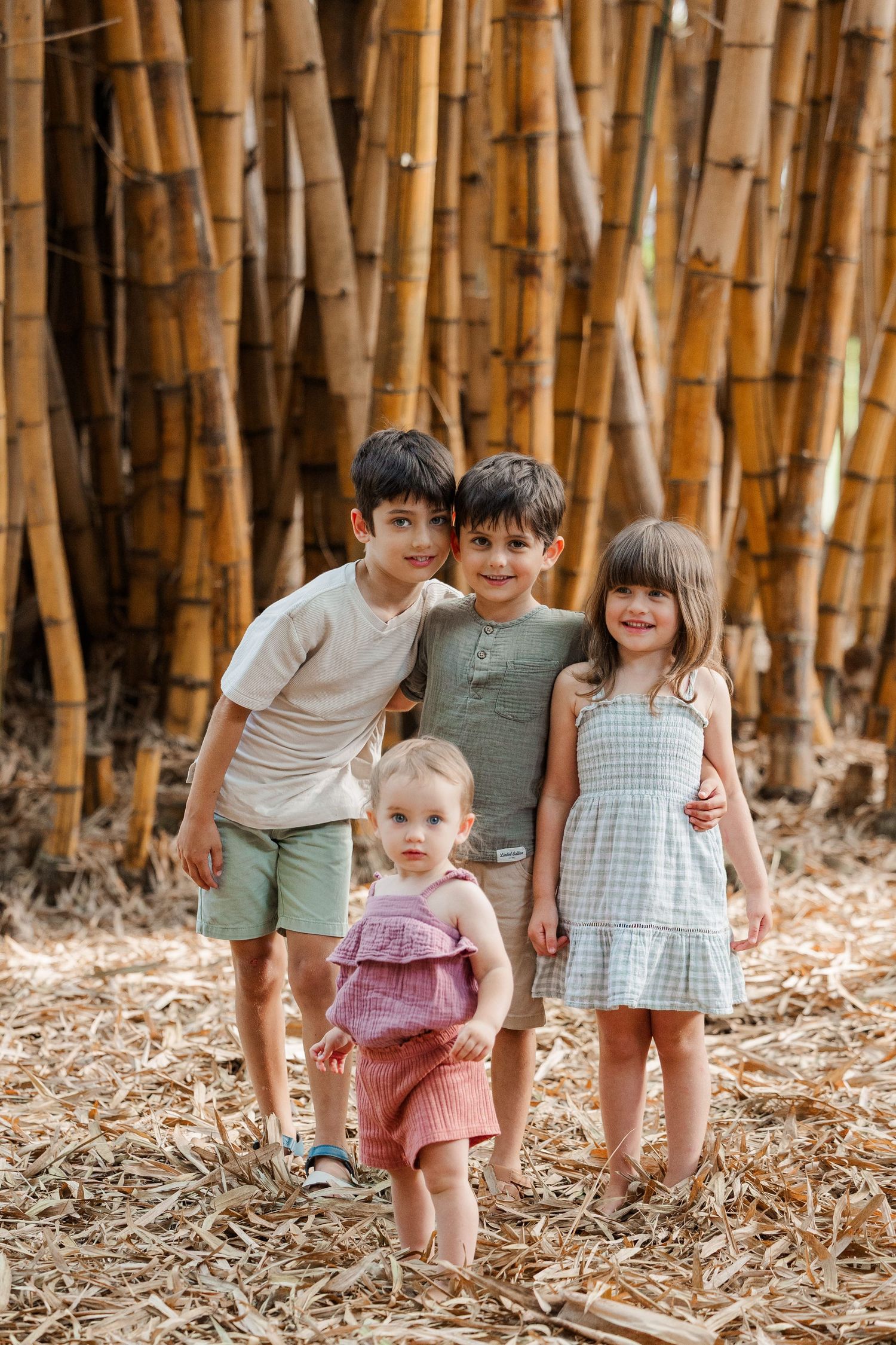Children explore a bamboo forest together while wearing coordinated pastel outfits on a sunny day.