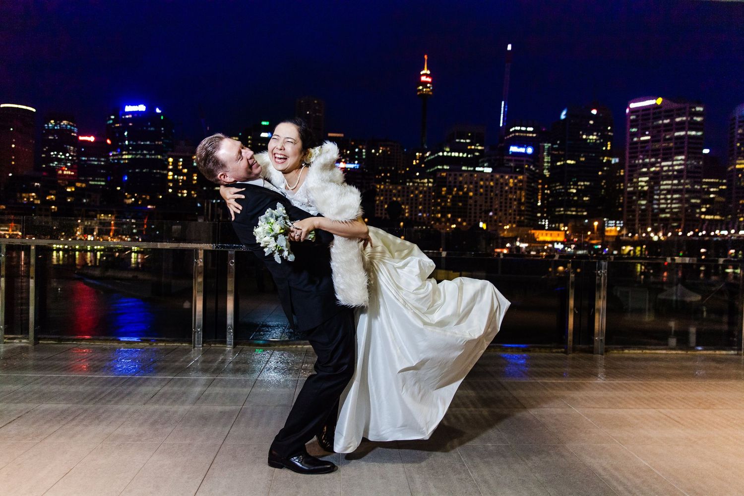 A romantic dance dip pose at night with the illuminated Sydney skyline and harbour visible in the background.