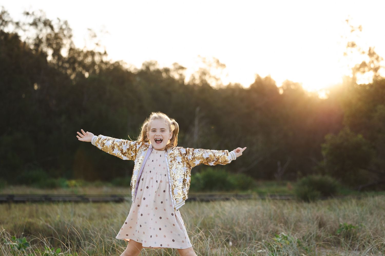 A joyful young girl with outstretched arms laughing in a golden sunlit field at sunset.