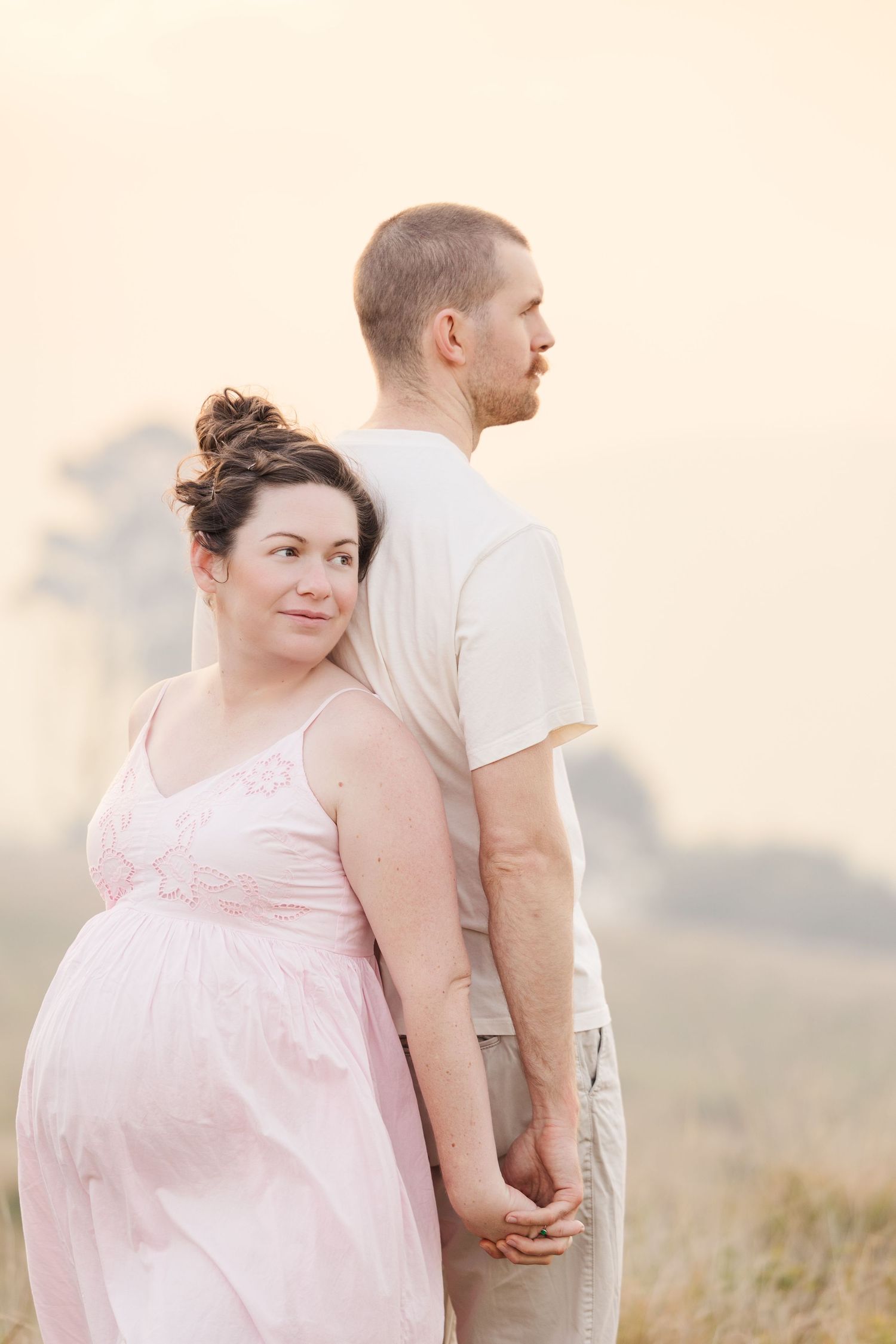 Couple in a sunlit field wearing white and pink outfits share intimate moments during a romantic photoshoot.