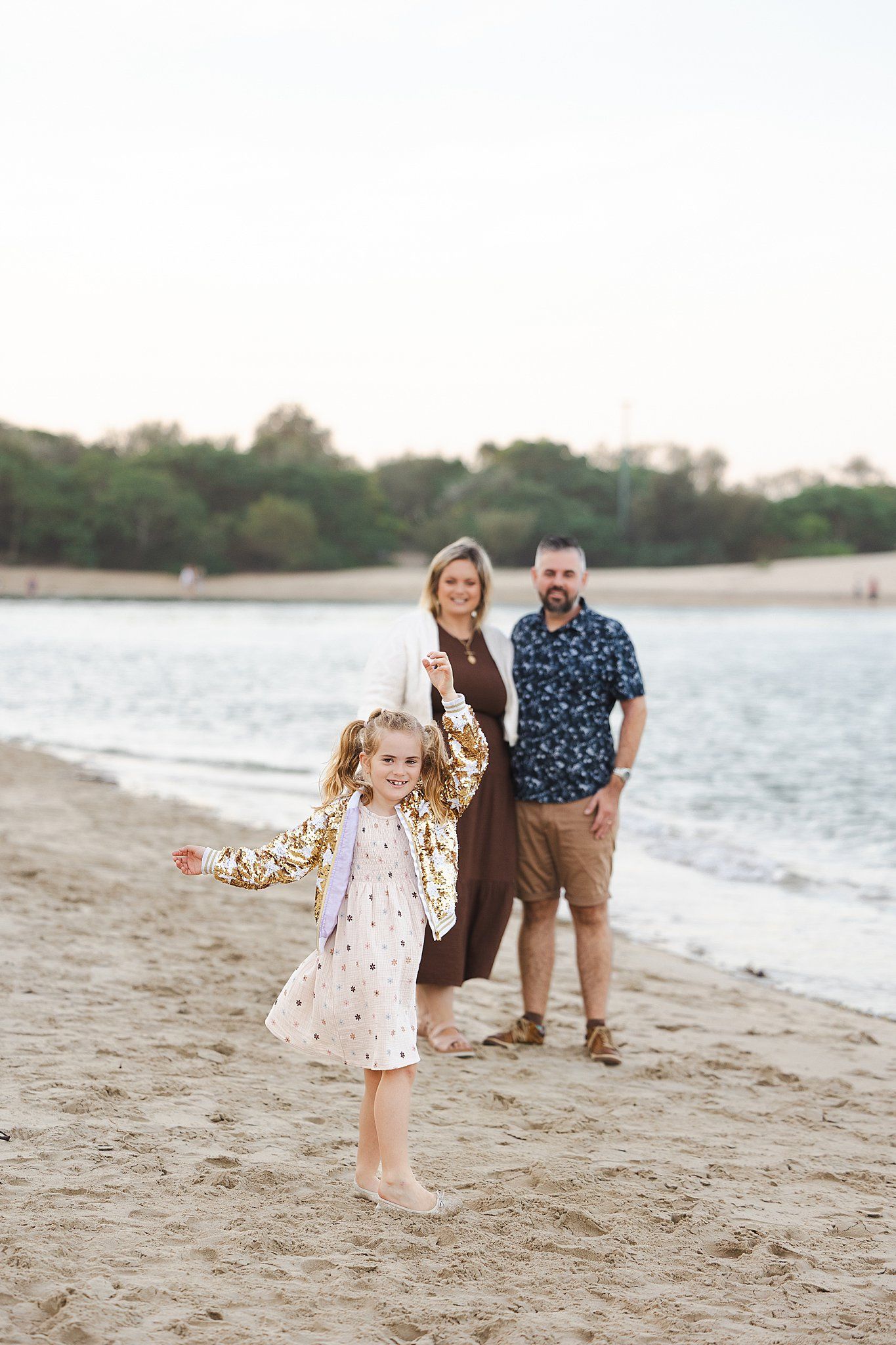 A family enjoys quality time together on a sandy beach at sunset with trees in the background.