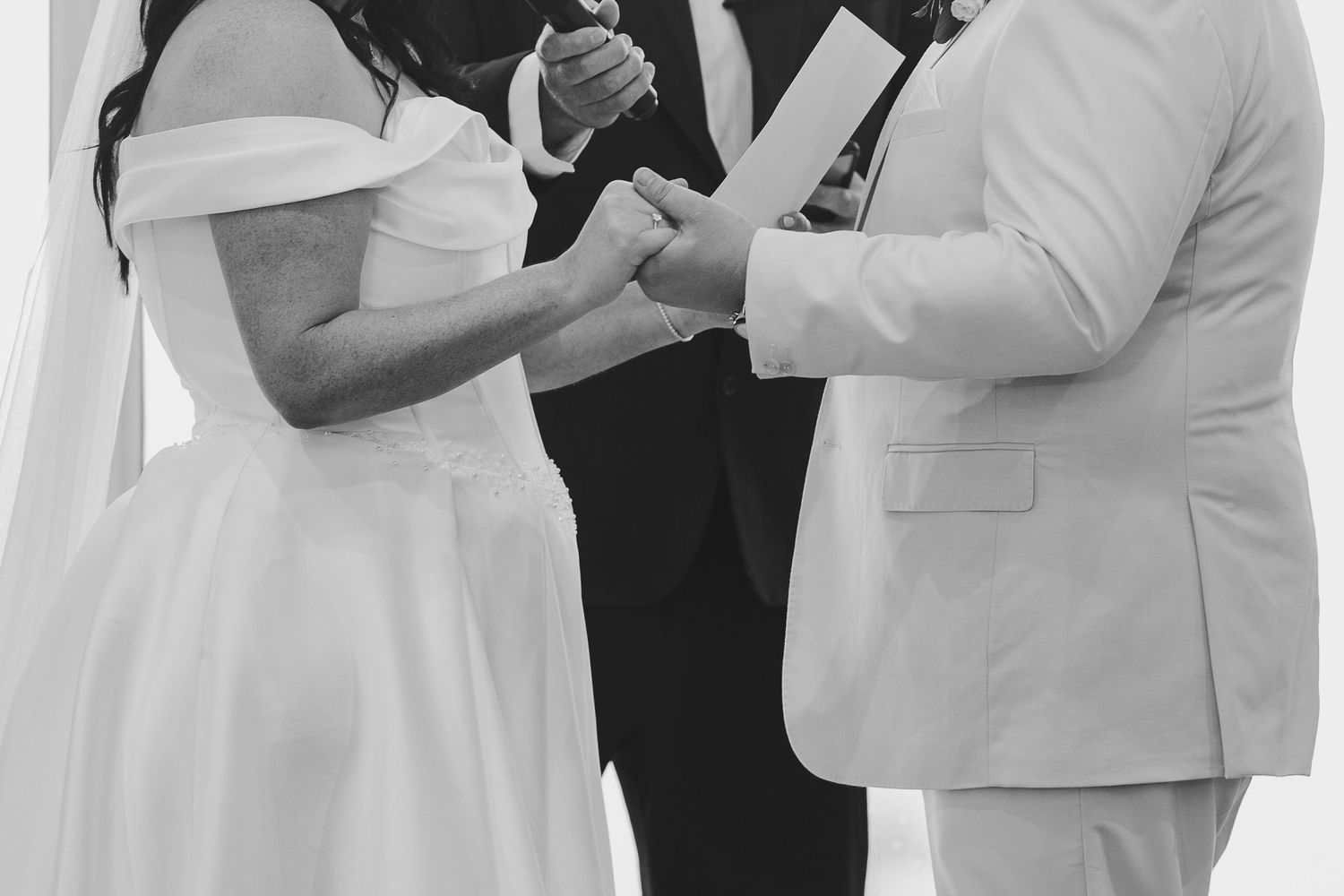 Black and white wedding ceremony photo of bride and groom exchanging rings before officiant.